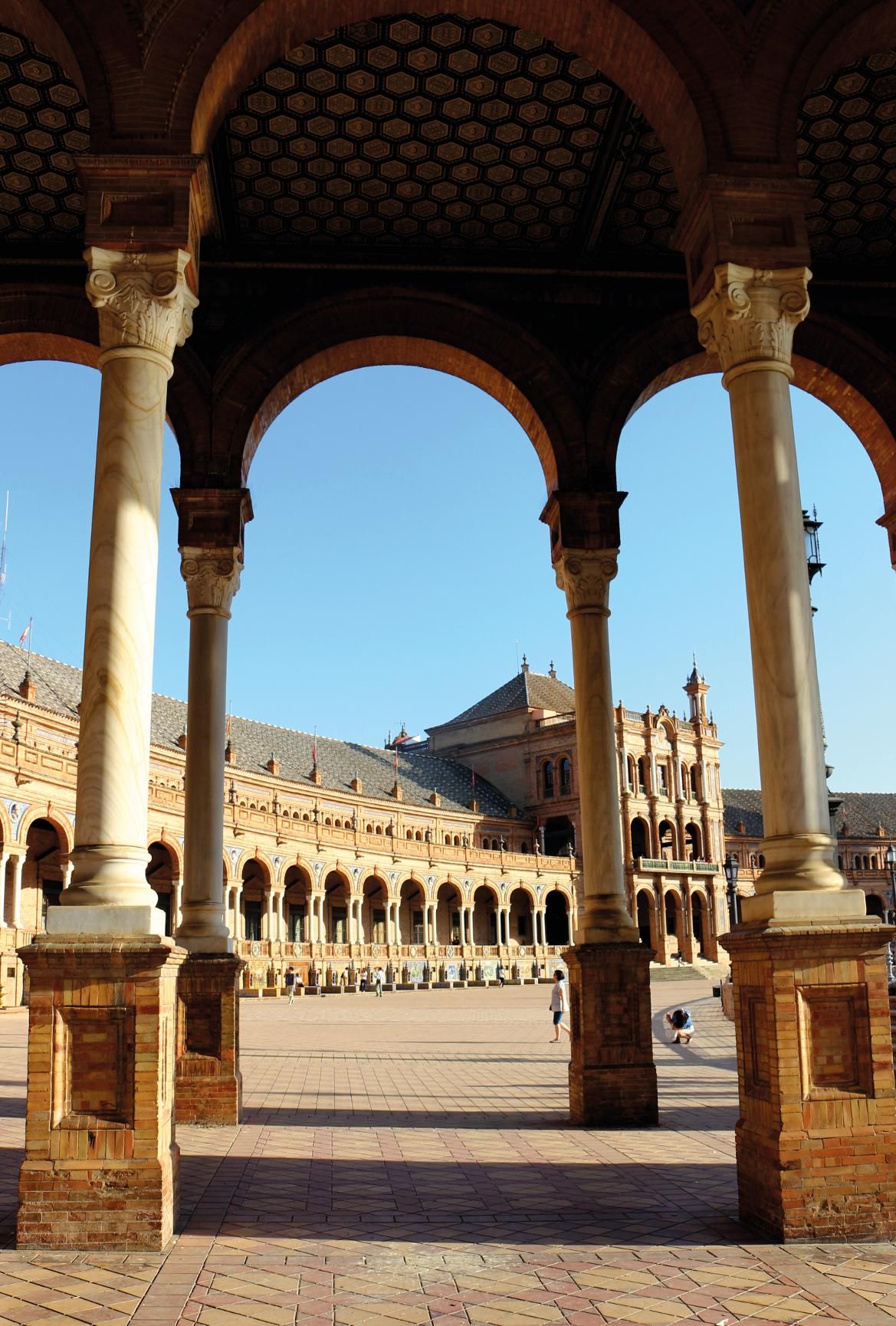 Ein Blick durch Arkaden auf einen weitläufigen Platz mit beeindruckender Architektur und klarem Himmel.