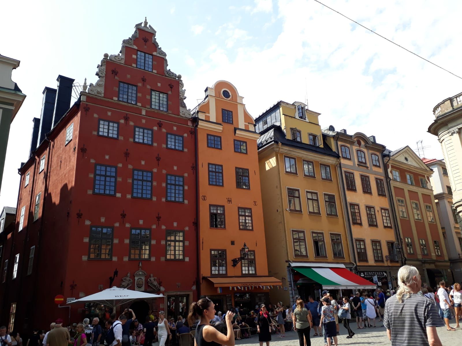 Bunte, historische Gebäude in einer lebhaften Straße, umgeben von Touristen und einem klaren blauen Himmel.