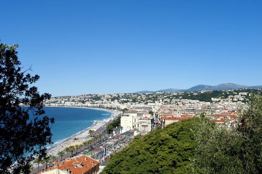Blick auf die Küste von Nizza mit blauem Himmel, Strandpromenade und Bergen im Hintergrund. Wunderschönes Panorama!