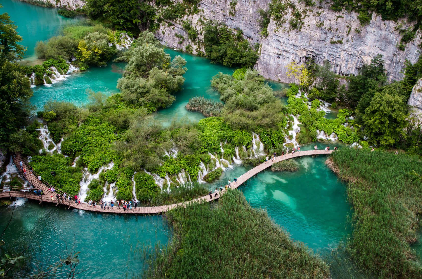 Wunderschöne Natur im Nationalpark Plitvice mit türkisblauem Wasser, plätschernden Wasserfällen und Holzstegen, die durch die Landschaft führen.