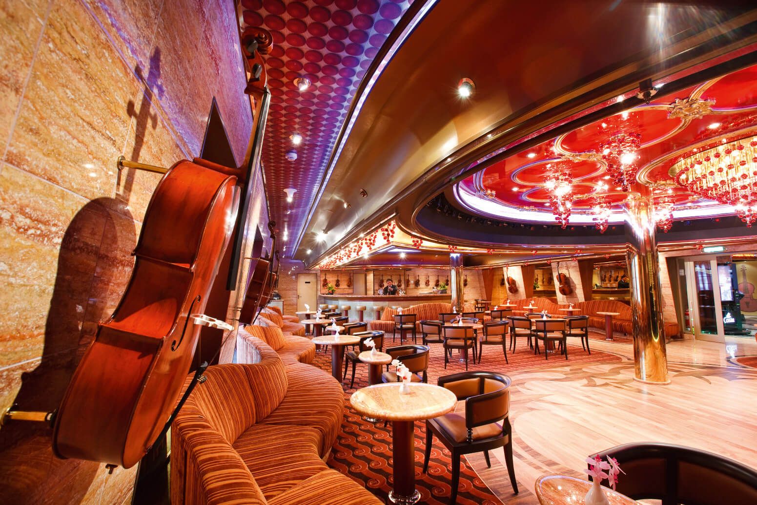 Elegantes Café mit roten Akzenten, Celli an der Wand und komfortablen Sitzplätzen für Gäste. Atmosphärisches Licht.