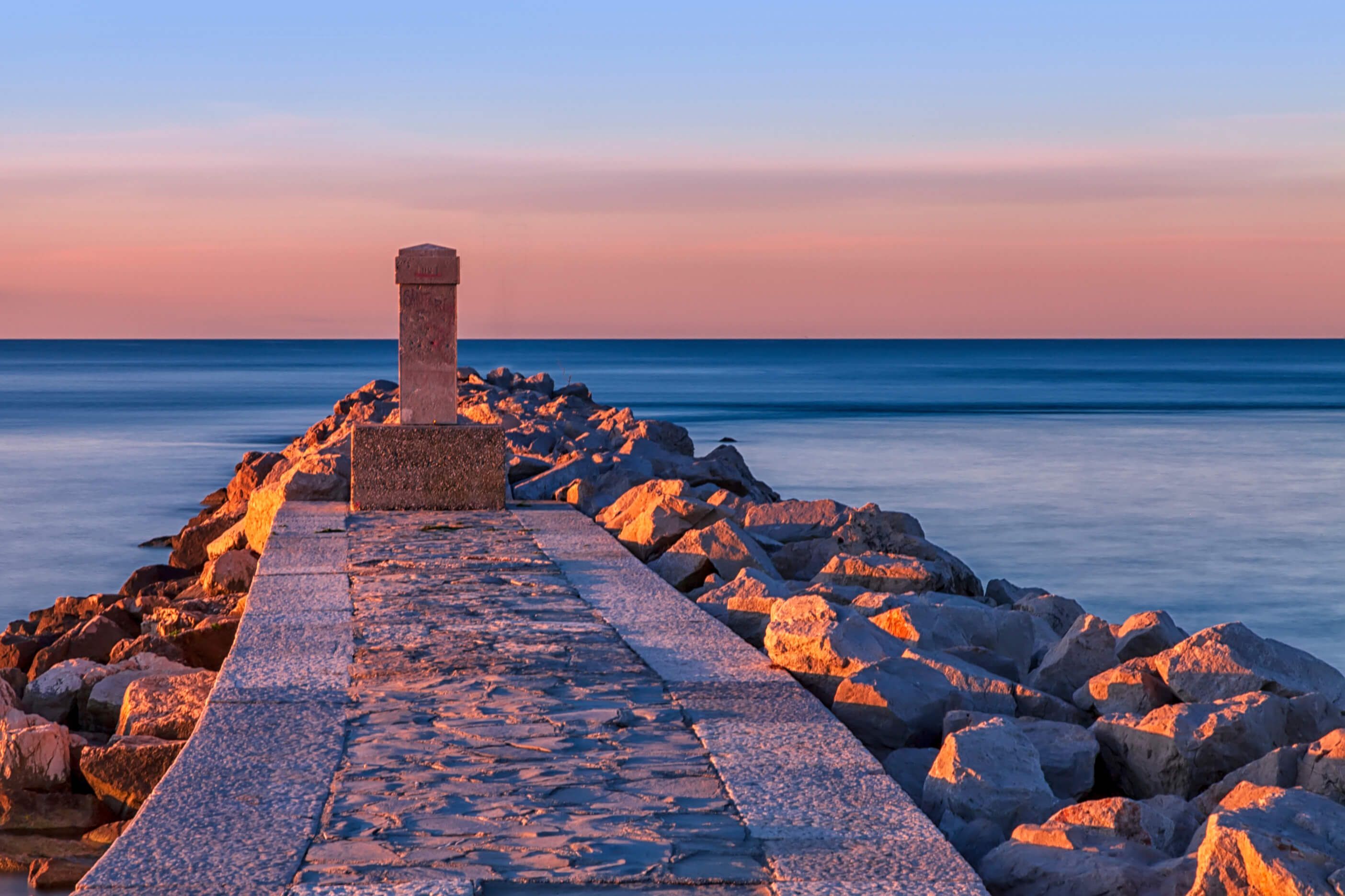 Ein steiniger Weg führt zu einem ruhigen Wasser, während der Sonnenuntergang sanfte Farben präsentiert.