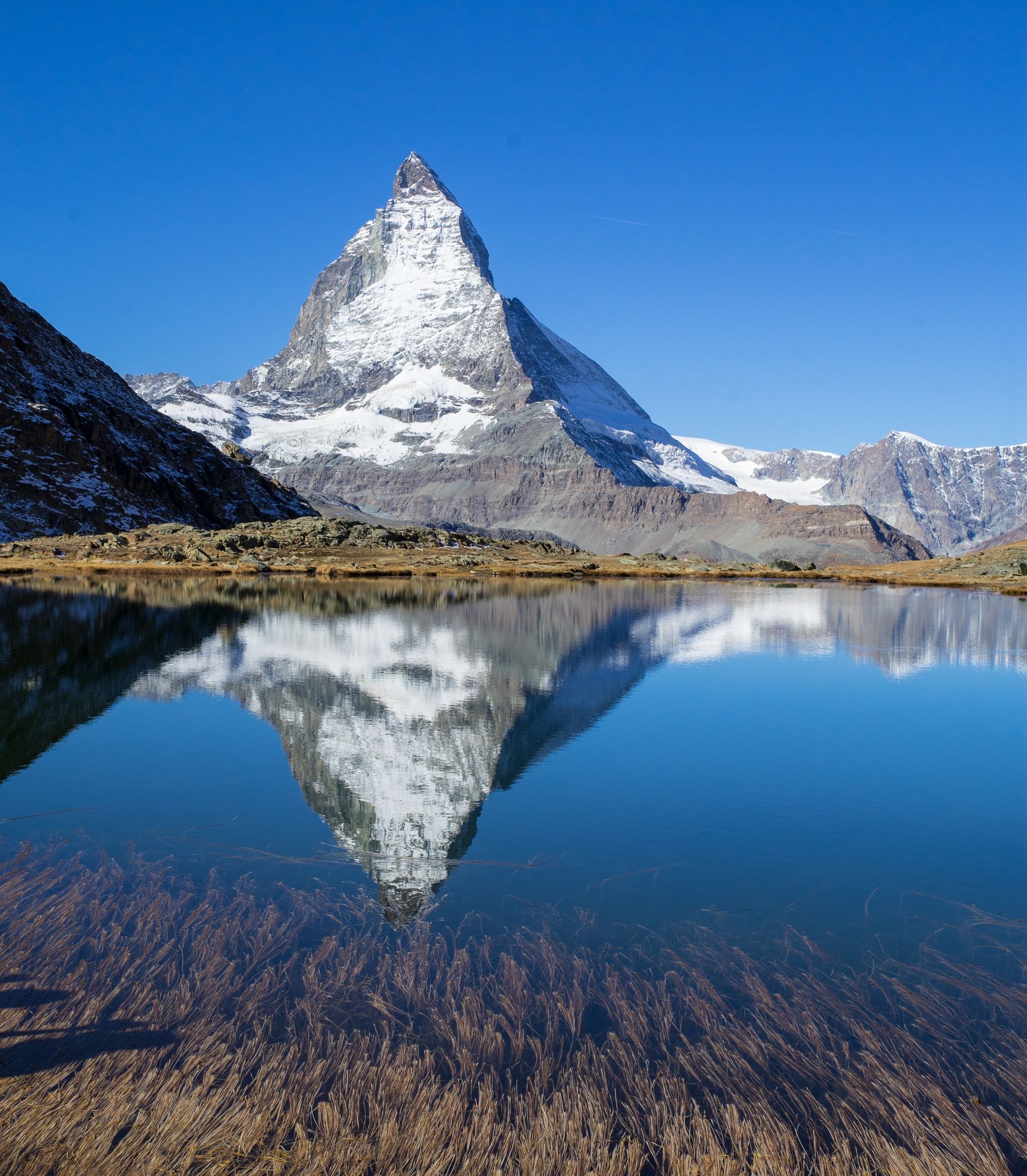 Das Bild zeigt das Matterhorn mit Spiegelung im klaren Wasser und umgeben von einer beeindruckenden Berglandschaft.