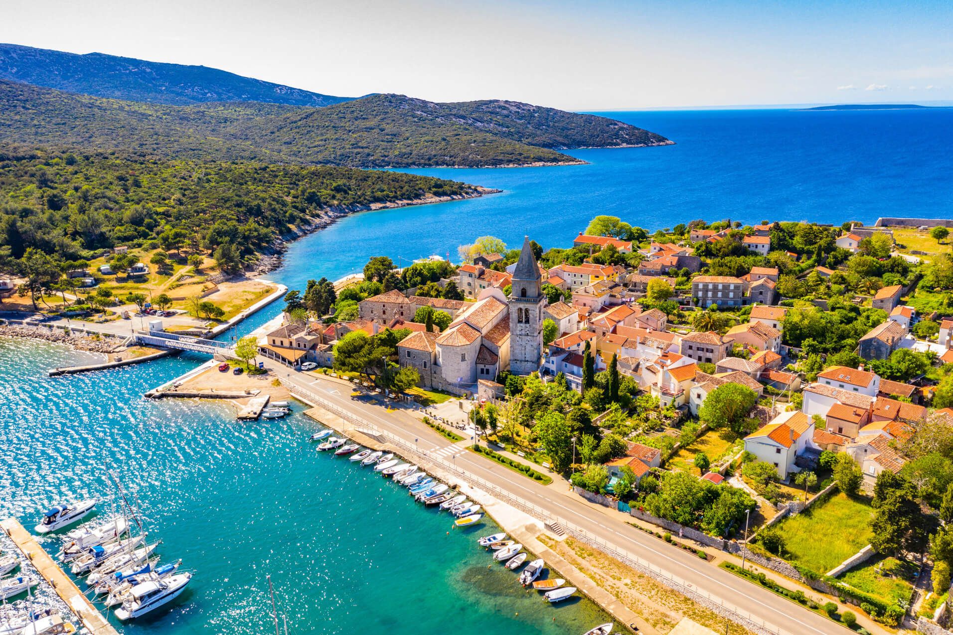 Malersches Küstendorf mit Hafen, blauem Wasser und grünen Hügeln, ideal für Erholung und Erkundung.