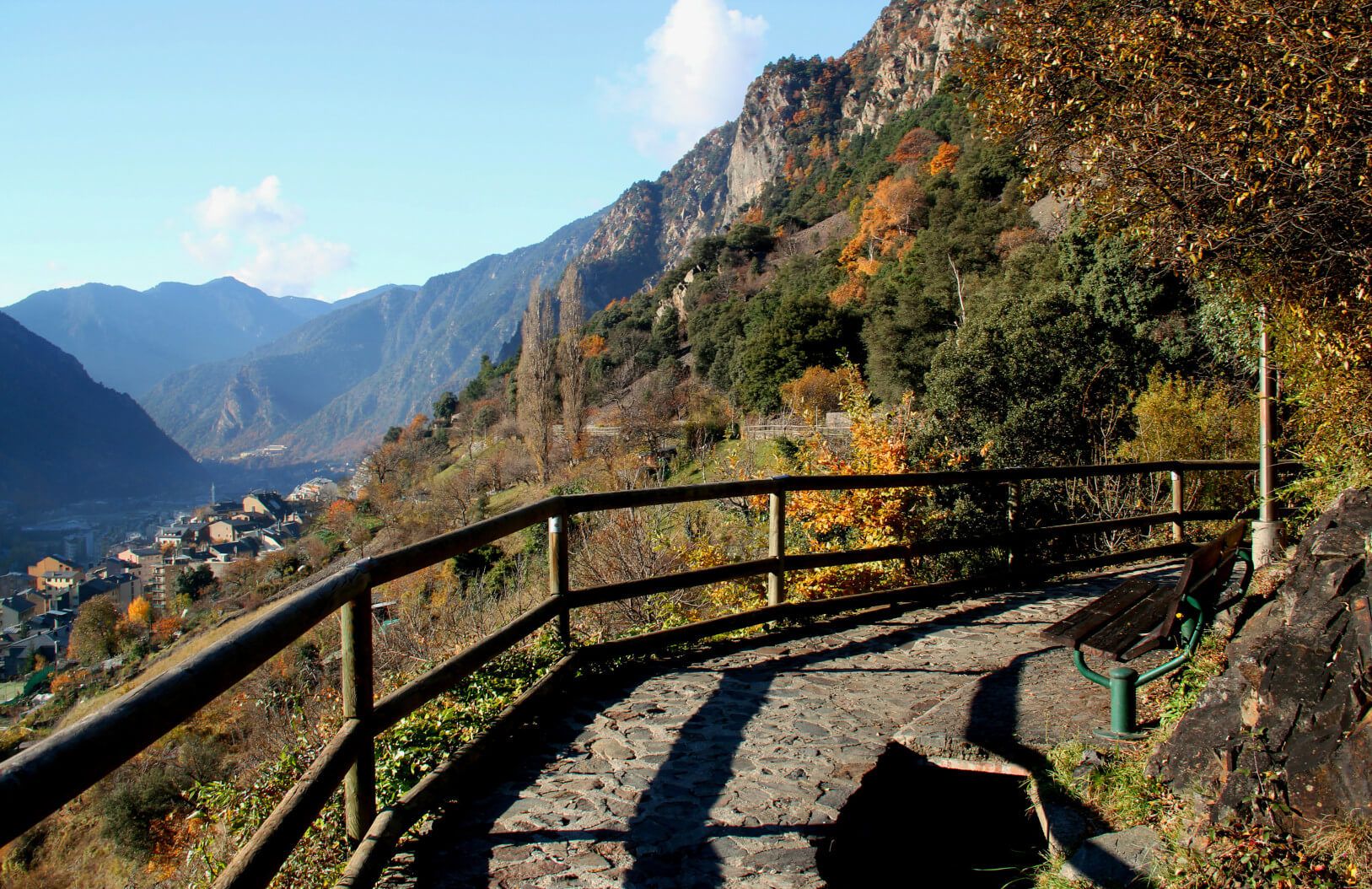 Eine Aussicht auf Berge und Täler, umgeben von buntem Herbstlaub und einem Weg mit Bank.