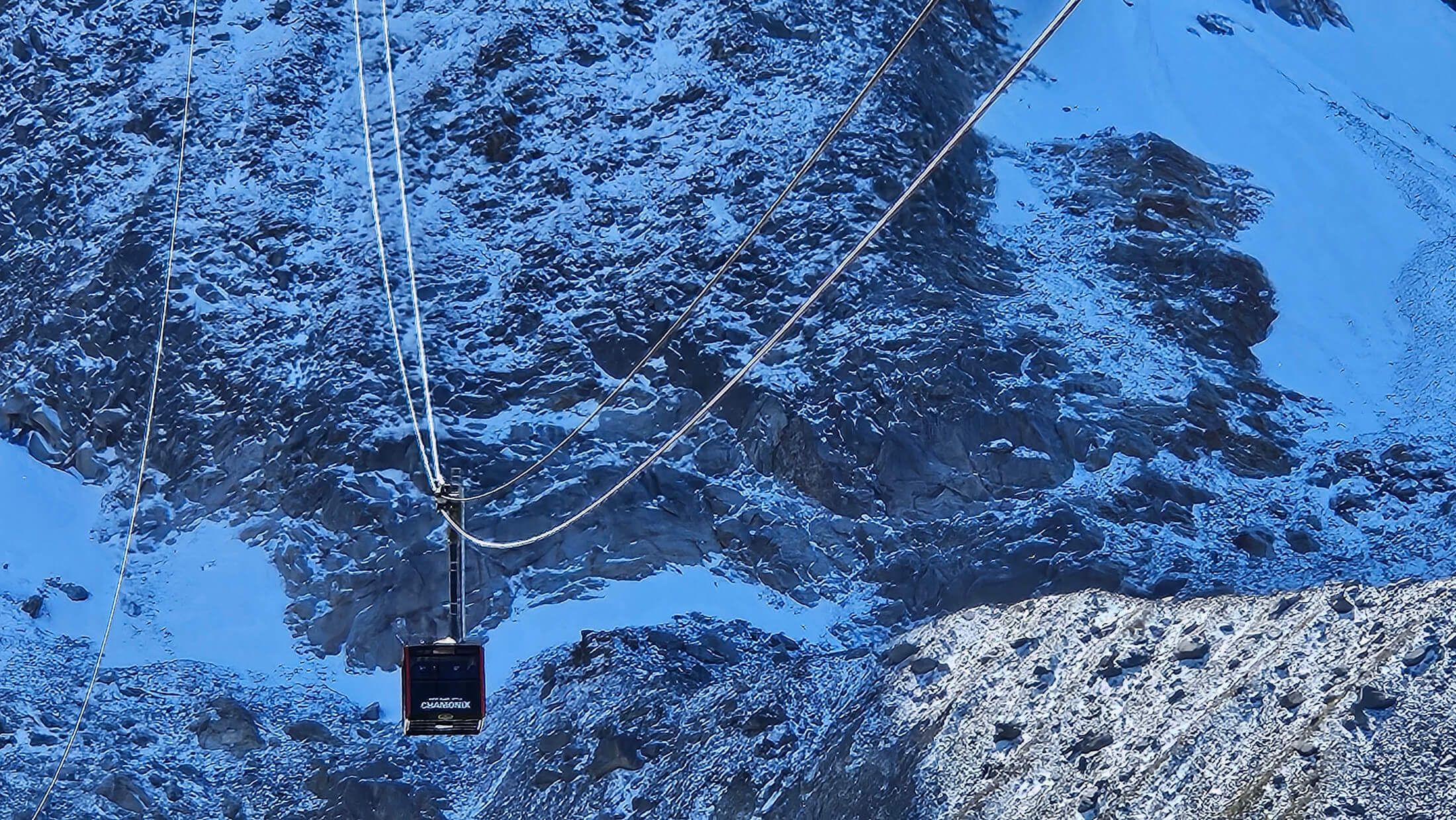 Eine Seilbahn schwebt über schneebedeckte Berge unter klarem, blauem Himmel.
