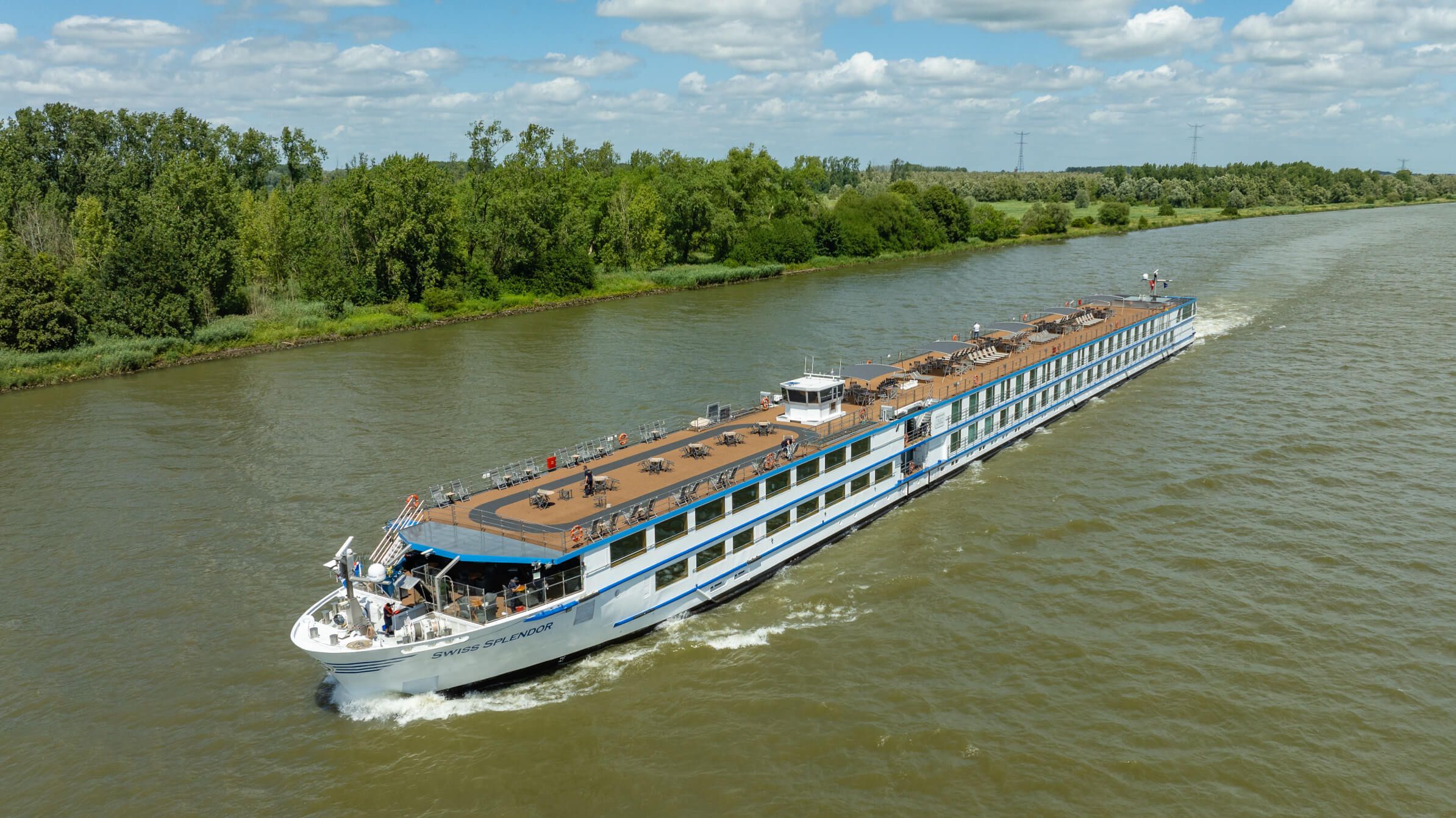 Ein luxuriöses Riverboat fährt gemächlich durch einen grünen Fluss, umgeben von üppiger Natur und blauen Himmel.