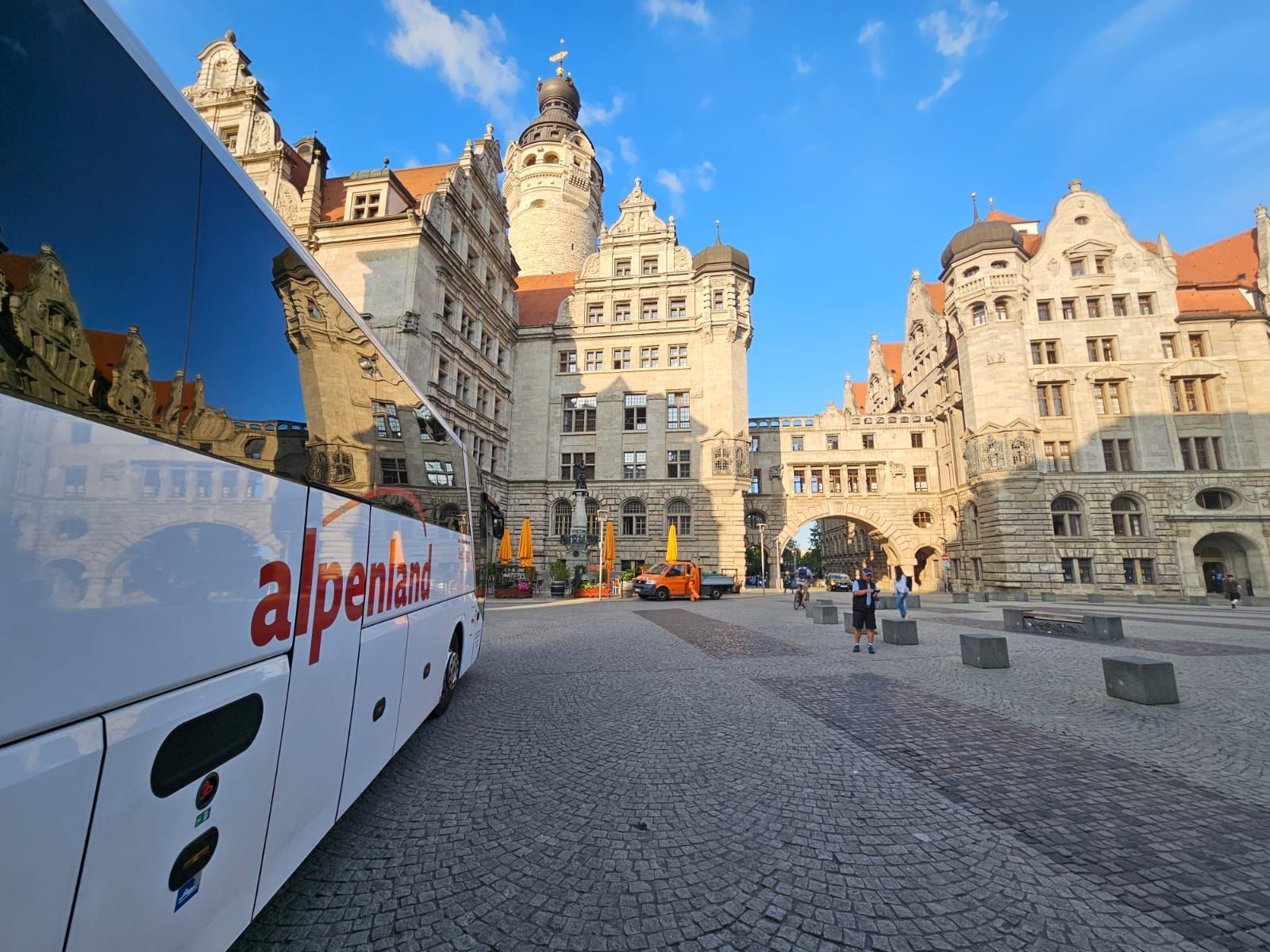 Ein Alpenland Bus parkt vor einem historischen Gebäude mit schöner Architektur und blauen Himmel im Hintergrund.