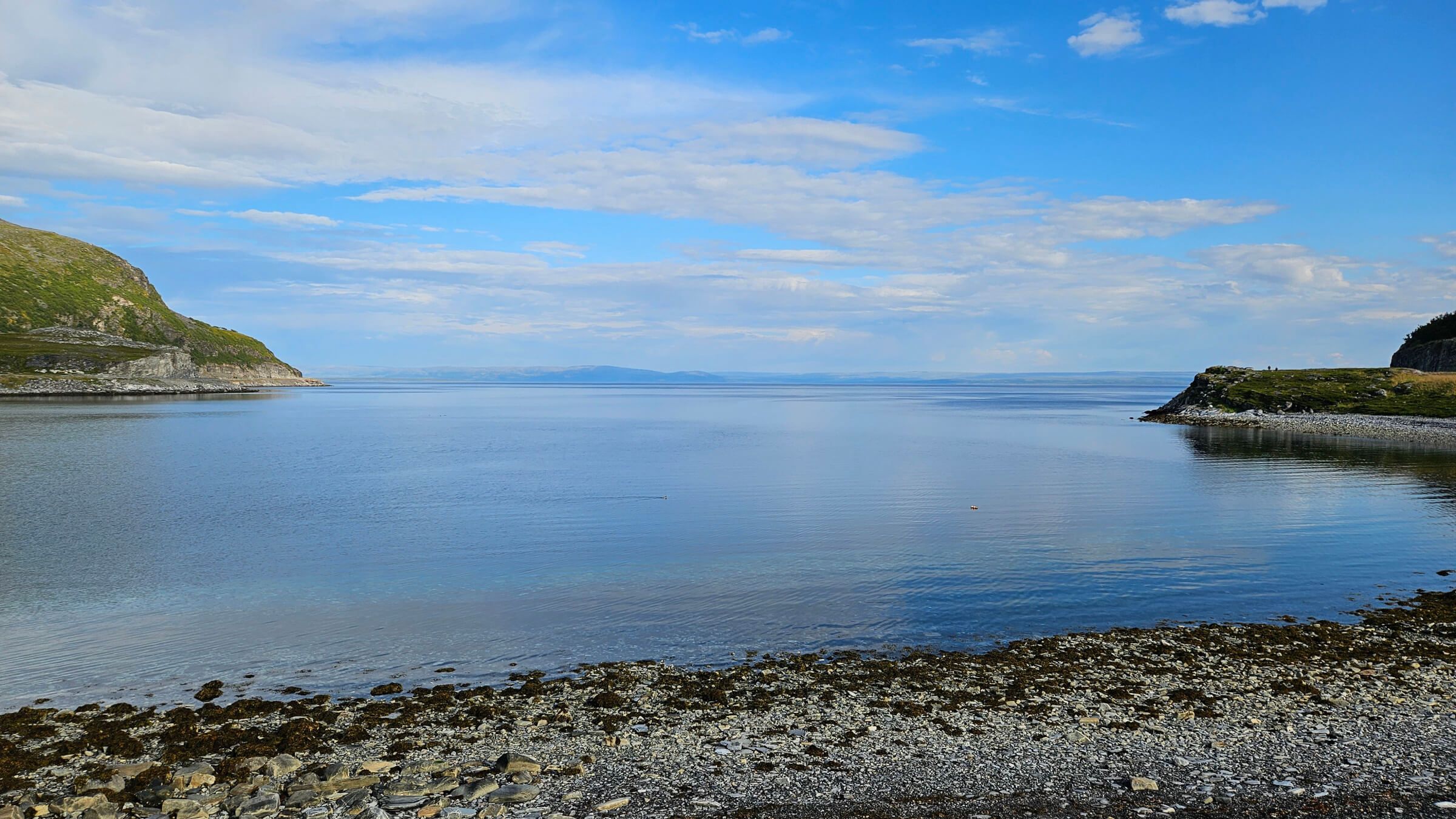 Ruhiger Gewässerblick mit klarem Himmel, umgeben von Hügeln und Steinen. Ideal für Entspannung und Naturgenuss.