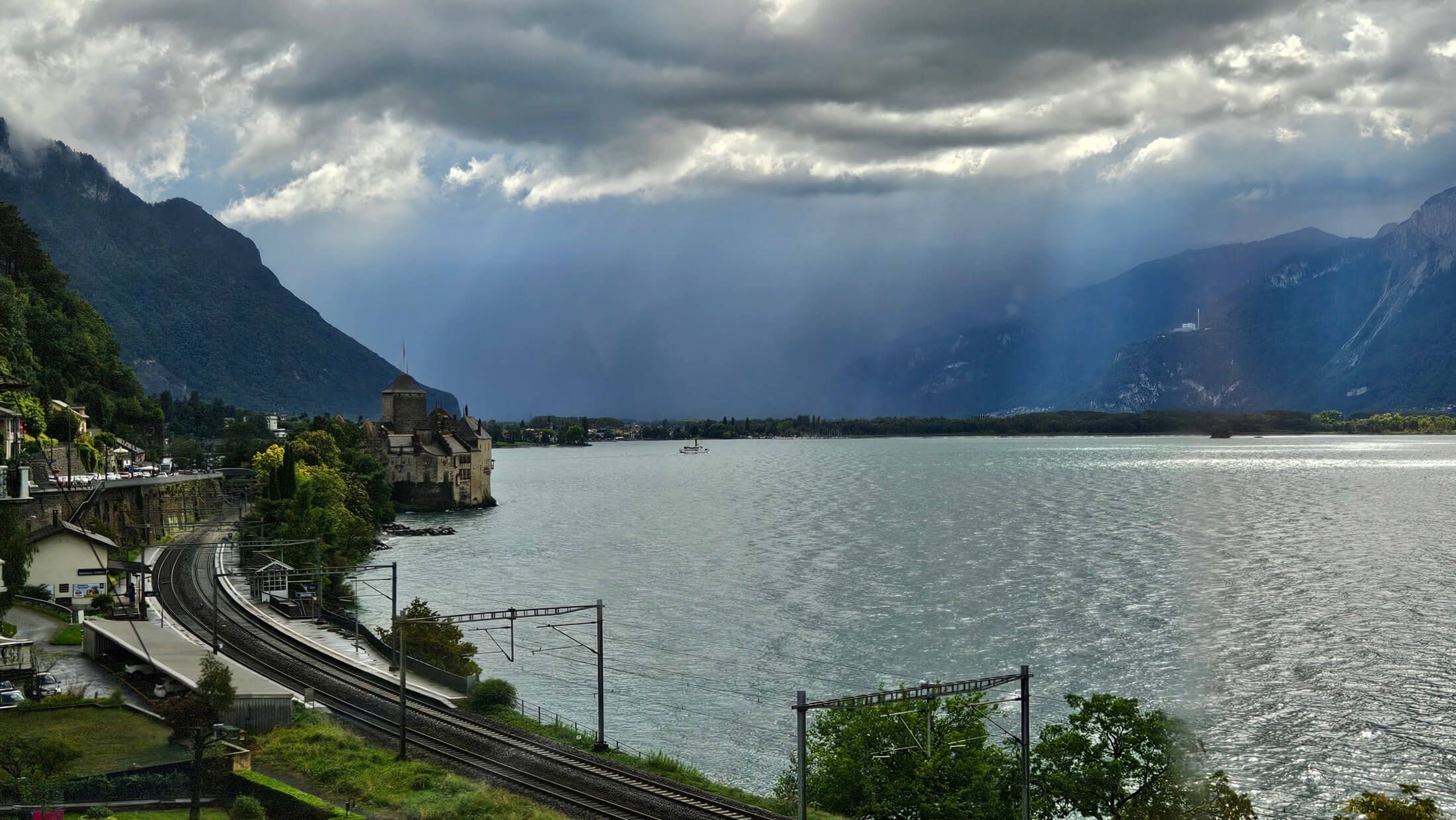 Ein malerischer See mit Bergen und einem historischen Gebäude, umgeben von dramatischen Wolken und sanftem Licht.