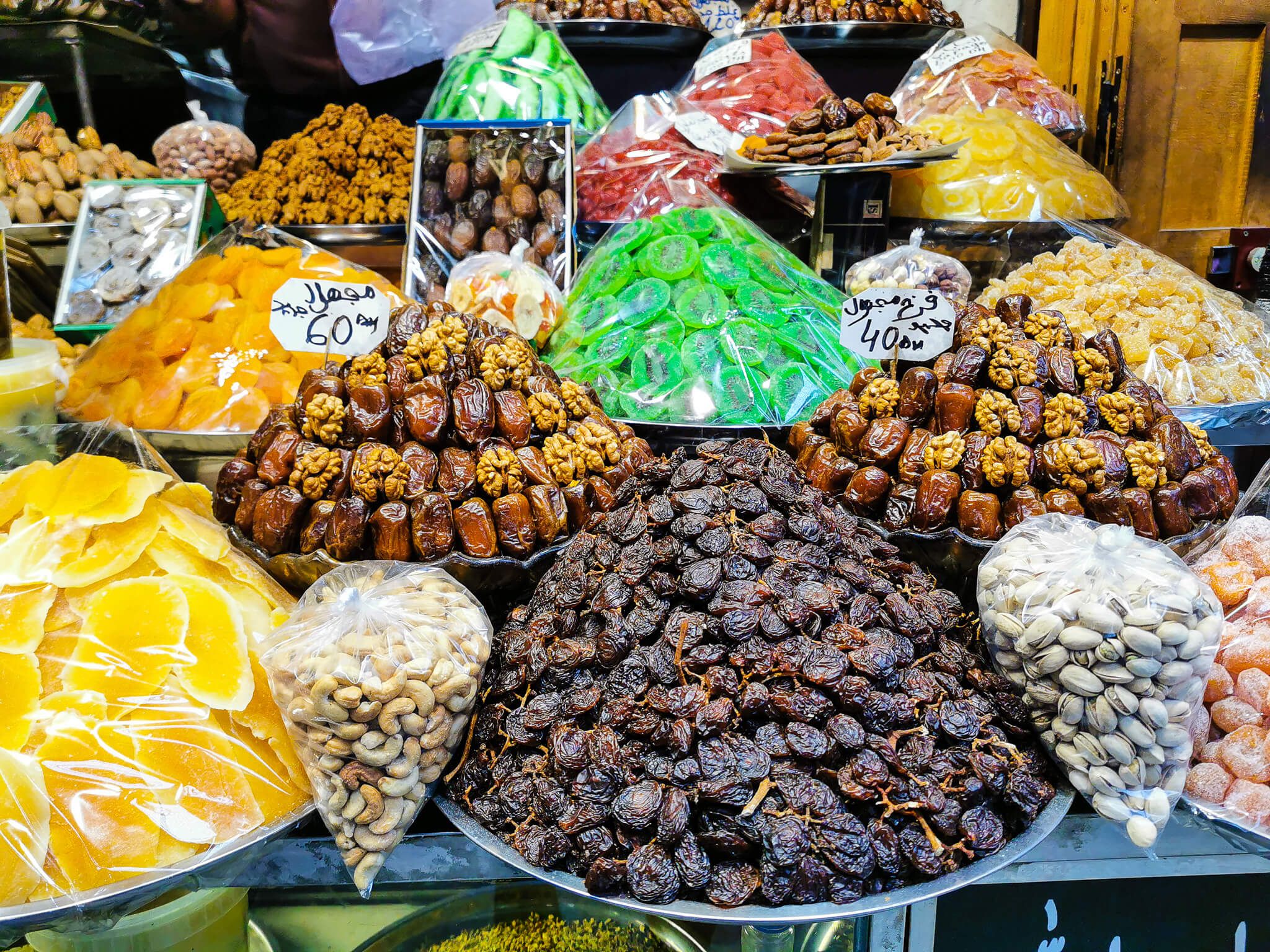 Bunte Auswahl an Trockenfrüchten und Süßigkeiten auf einem Markt, mit Etiketten und verschiedenen Farben.