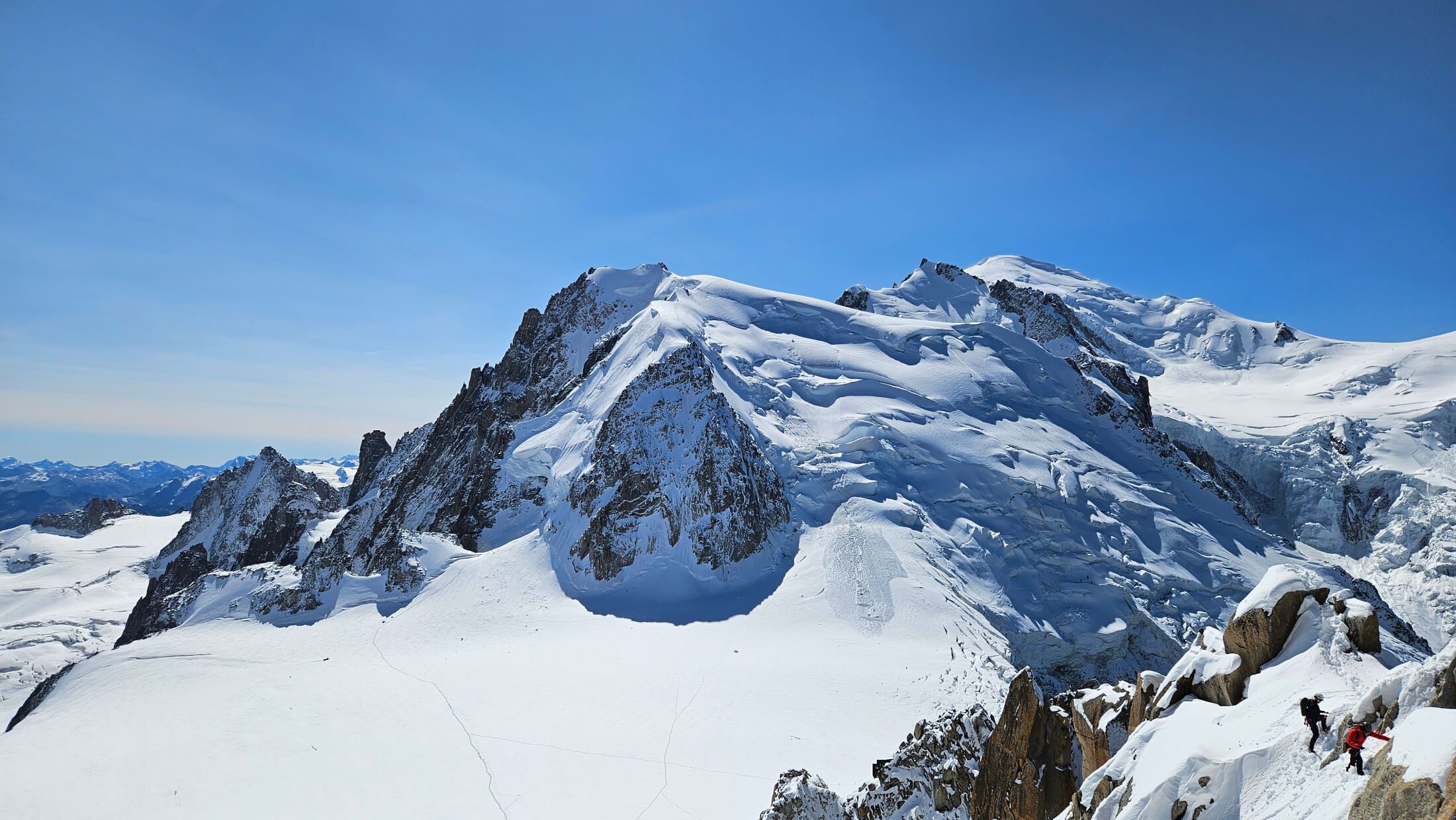 Schneebedeckte Berge unter klarem Himmel, Wanderer auf einem schmalen Pfad in der beeindruckenden Alpenlandschaft.
