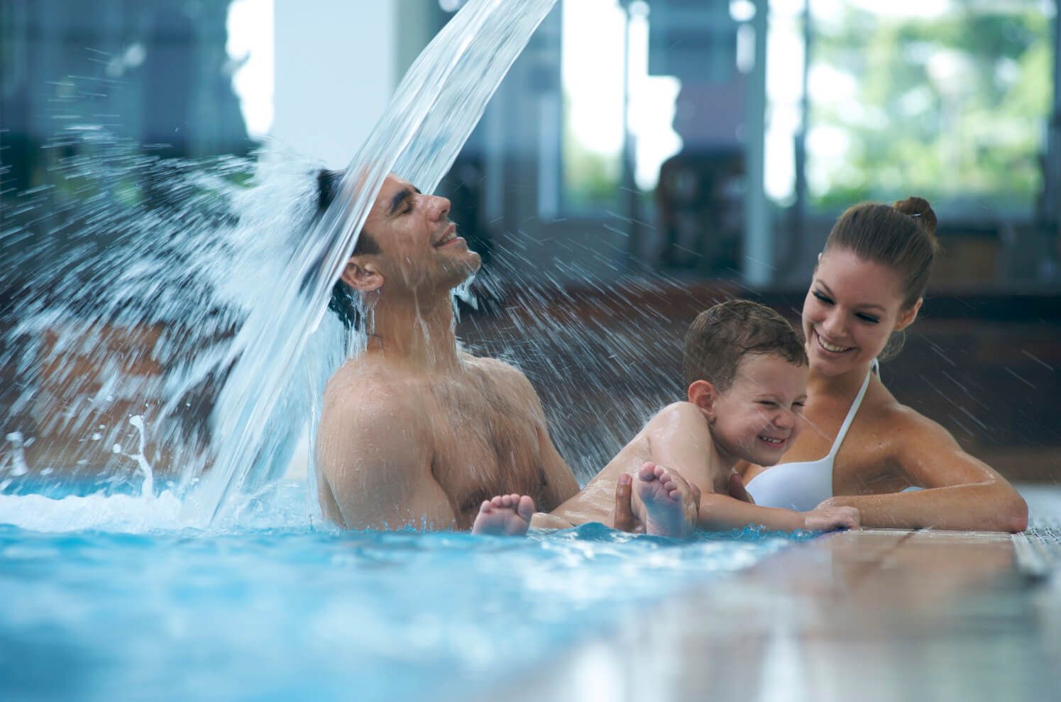 Eine fröhliche Familie spielt im Schwimmbad, Wasser spritzt, Gelächter und Spaß in der Luft.