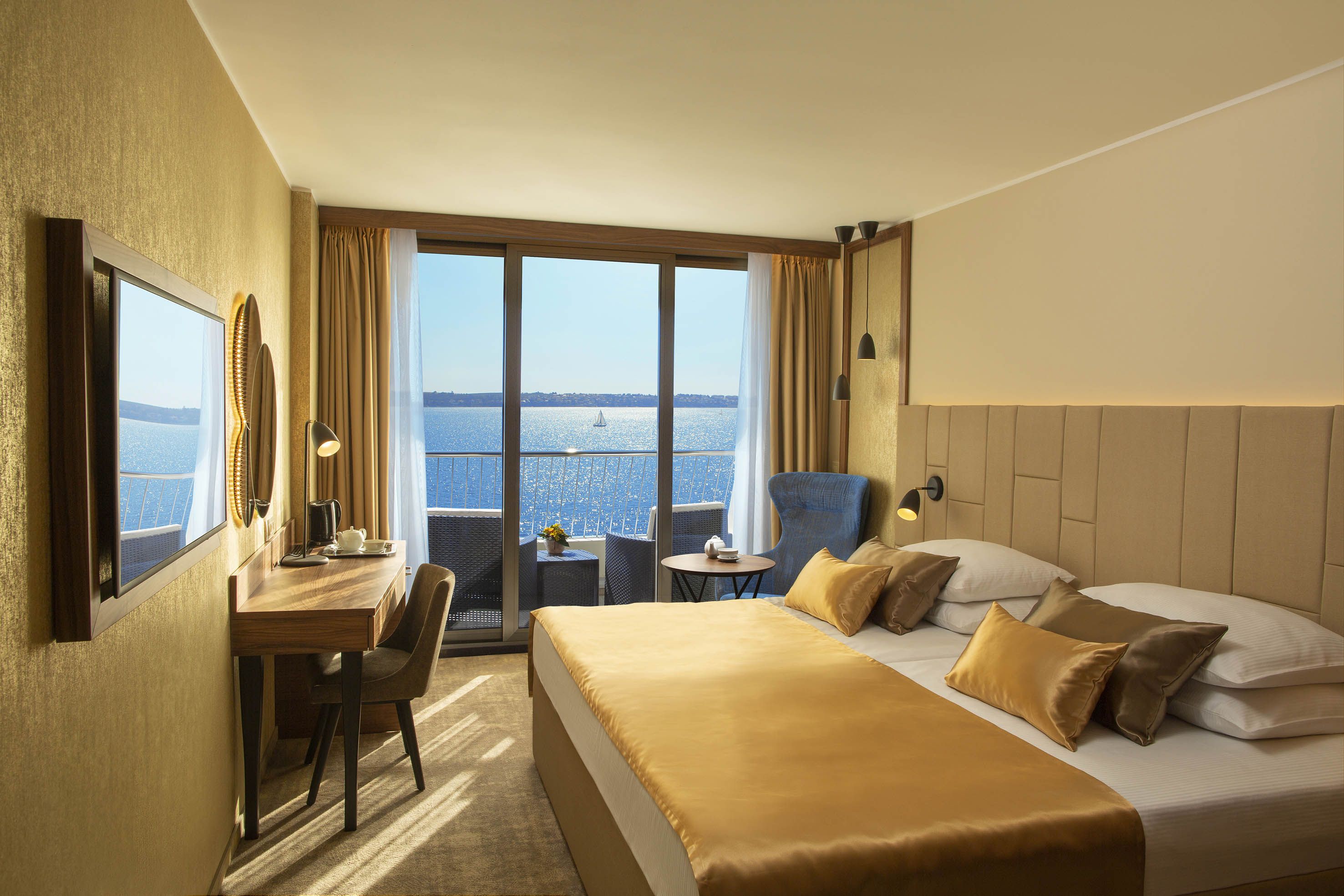 Elegantes Zimmer mit Blick auf das Wasser, goldenen Akzenten und gemütlicher Sitzecke auf dem Balkon.
