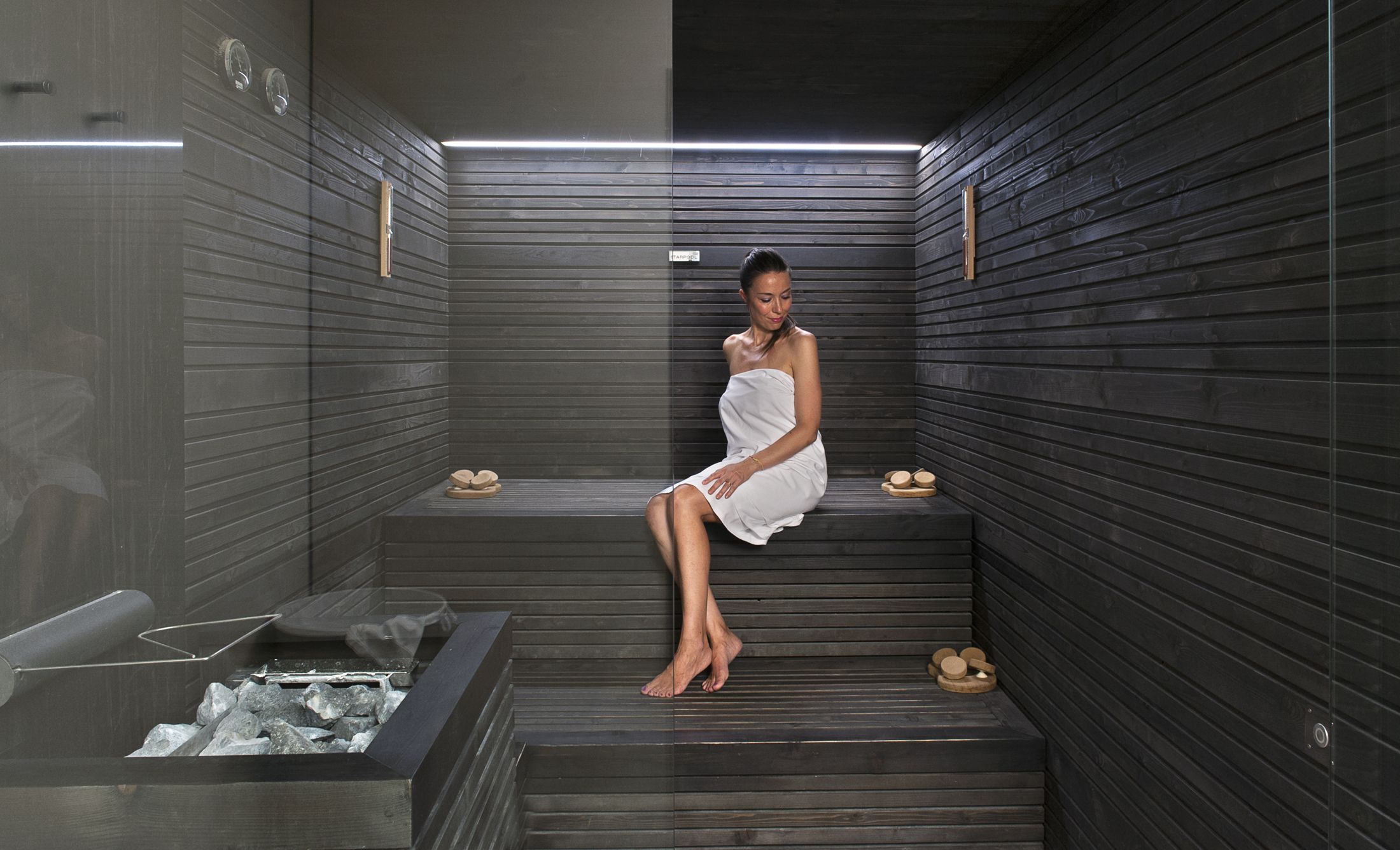 Eine elegante Frau in einem Handtuch entspannt in einer modernen Sauna mit dunklen Holzverkleidungen.