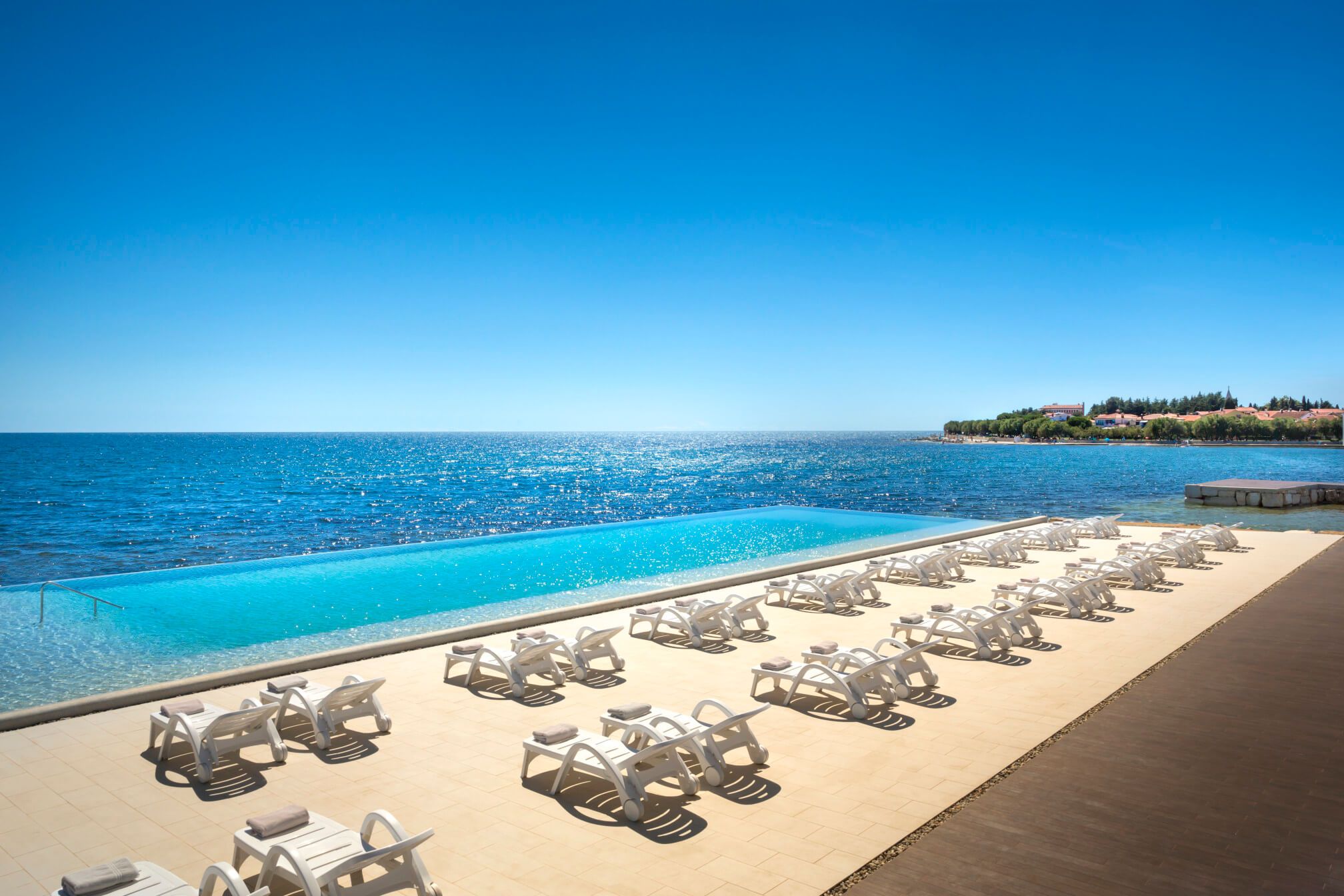 Ein schöner Swimmingpool mit Liegen, Blick auf das glitzernde Meer und einen wolkenlosen blauen Himmel.