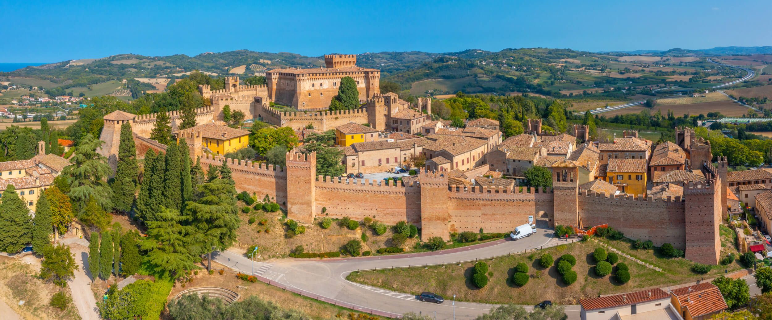 Eine weitläufige Burgenlandschaft umgeben von sanften Hügeln und blauem Himmel, mit historischen Gebäuden und grüner Natur.
