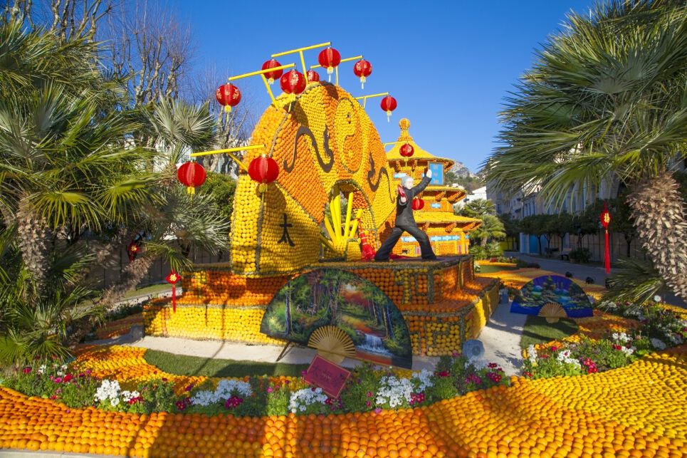 Eine bunte Festinstallation aus Früchten mit roten Laternen und Palmen an einem sonnigen Tag.