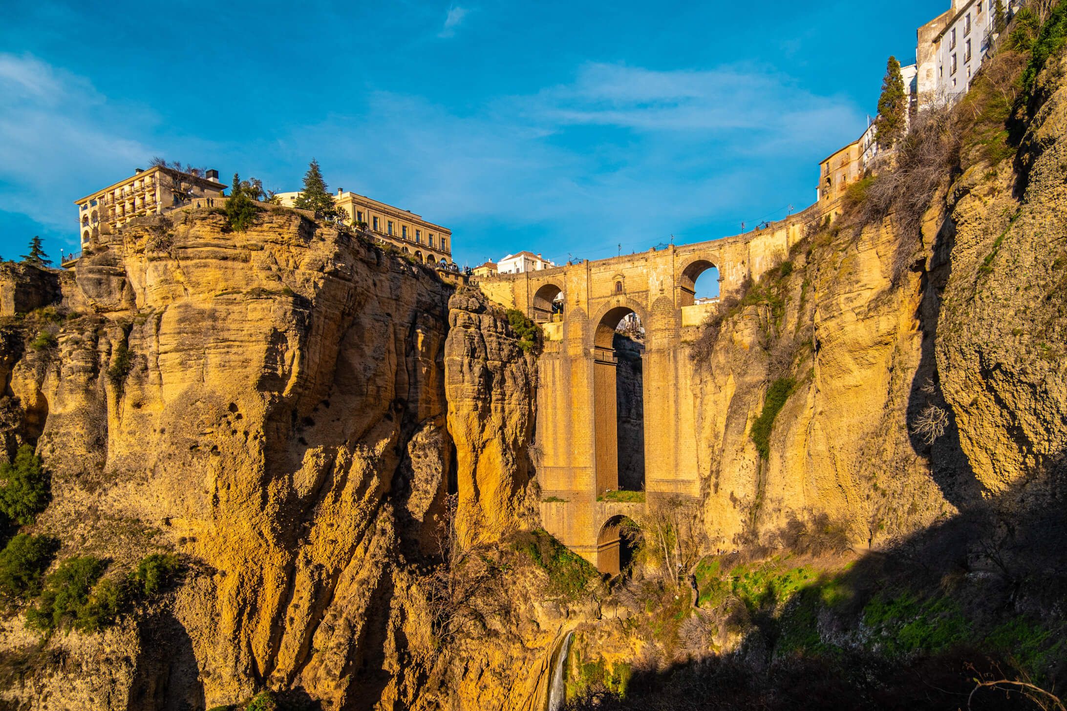 Die dramatische Klippe mit einer beeindruckenden Brücke und Gebäuden darunter bei klarem Himmel.