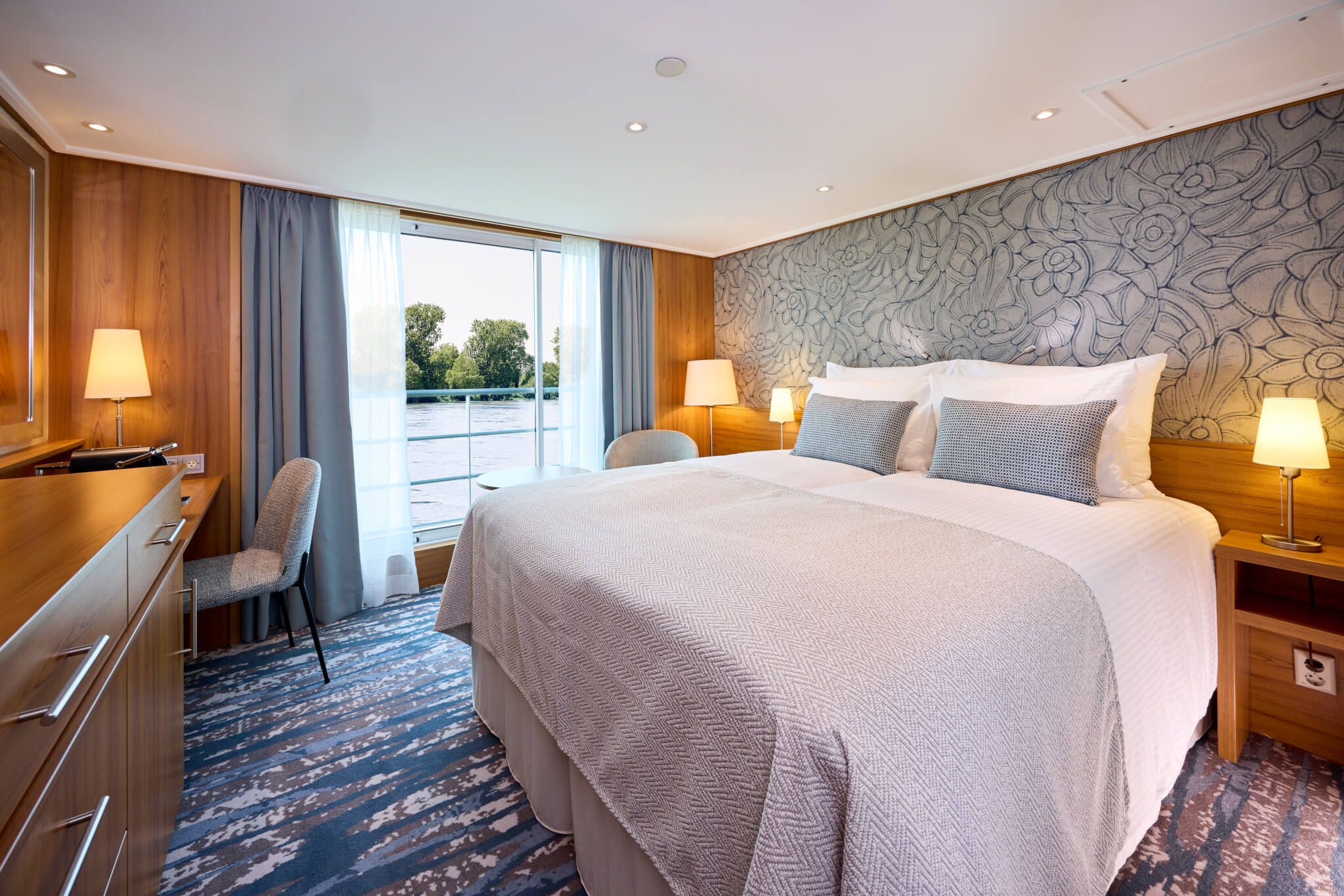 Ein modernes Zimmer mit Doppelbett, Holzdekor und Blick auf einen Fluss durch große Fenster. Gemütlich und einladend.