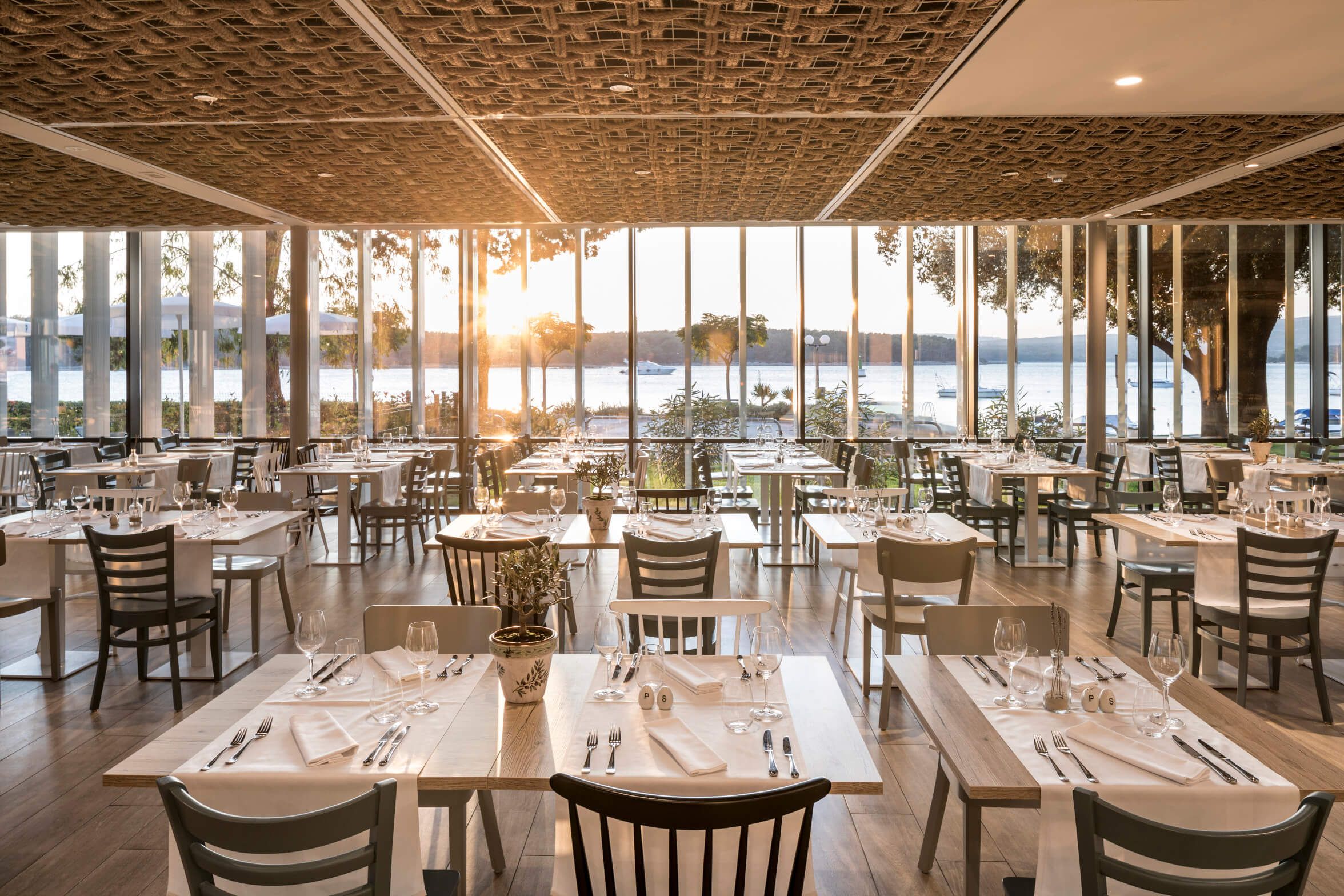Ein modernes Restaurant mit Blick auf den Sonnenuntergang und dekorierten Tischen am Wasser.
