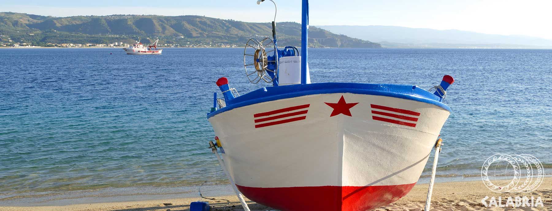 Ein buntes Boot steht am Strand, das klare Wasser reflektiert die Berge im Hintergrund. Nette Küstenstimmung!