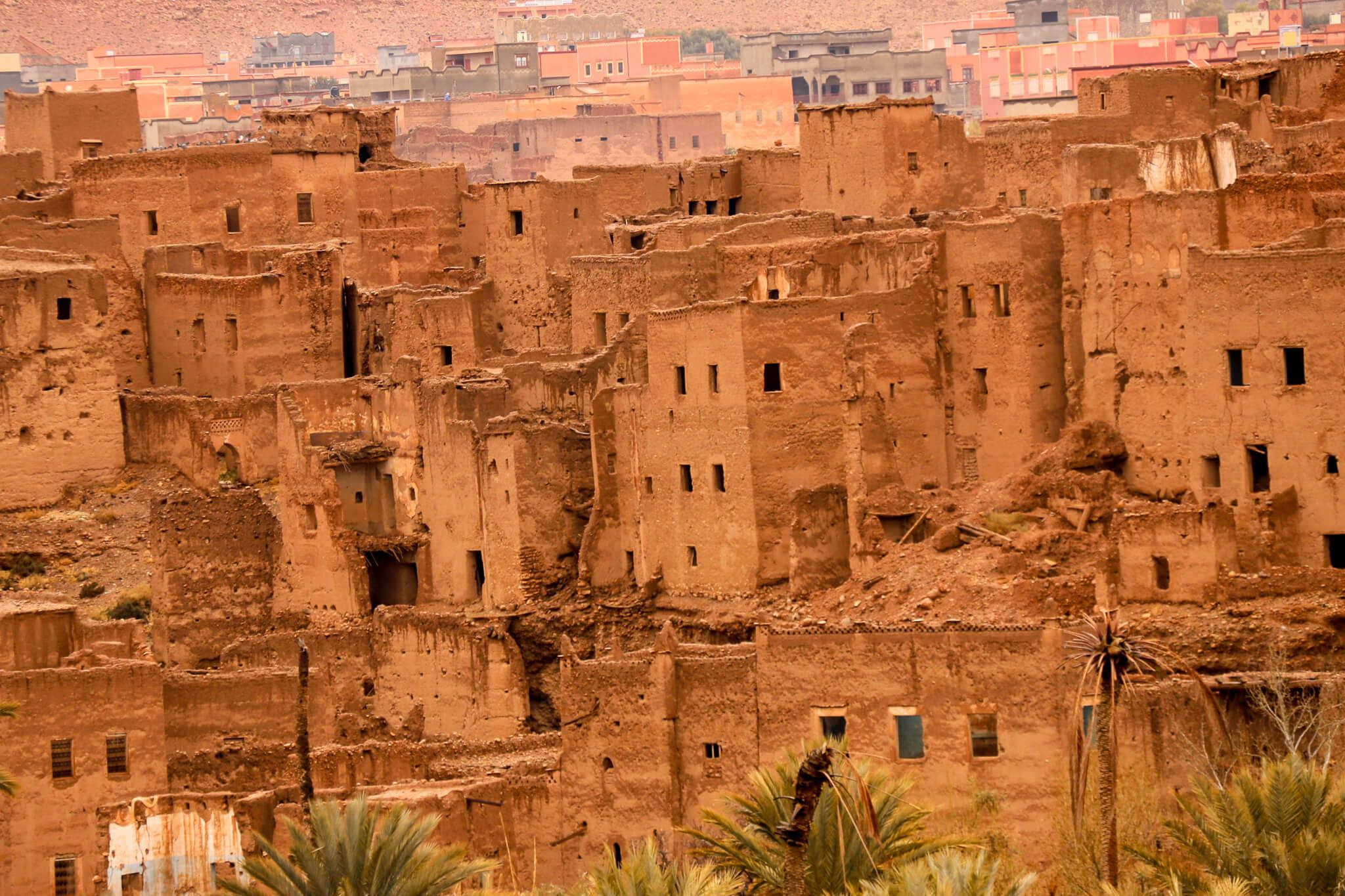 Ein verlassenes Lehmdorf mit zerfallenen Häusern und einer beeindruckenden Wüstenlandschaft im Hintergrund.