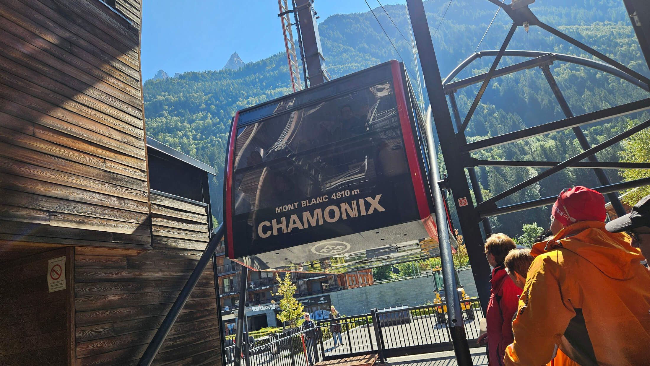 Eine Bergbahn in Chamonix, umgeben von grünen Bergen, warten mehrere Personen auf den Aufstieg.