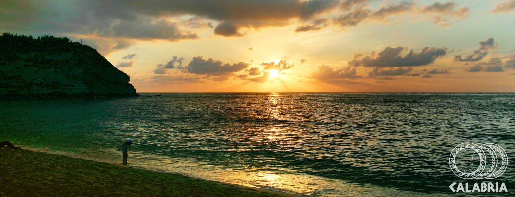 Sonnenuntergang über dem Meer, mit einem Kind am Strand und einer Felsenküste im Hintergrund.