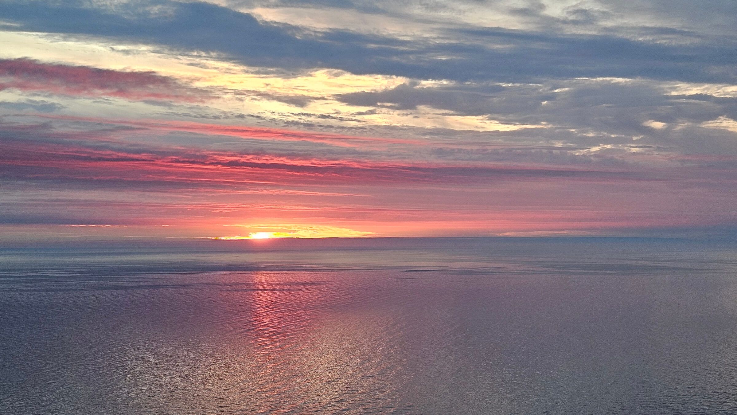 Ein beeindruckender Sonnenuntergang über dem stillen Wasser, mit bunten Wolken und sanften Reflexionen.