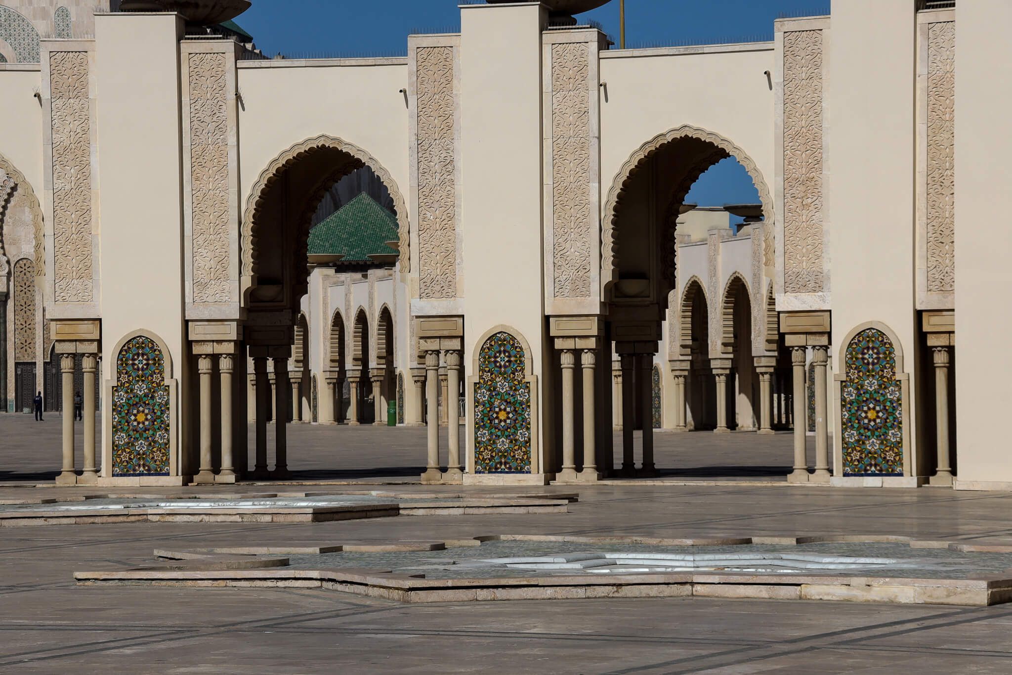 Eine architektonische Ansicht mit Bögen, Säulen und bunten Fenstern in einem hellen, offenen Raum.