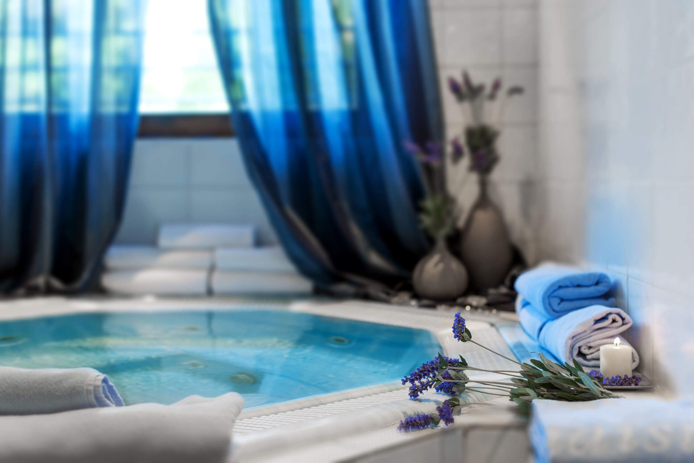 Ein eleganter Wellnessbereich mit einem blauen Whirlpool, Handtüchern und Lavendelblüten für Entspannung und Ruhe.