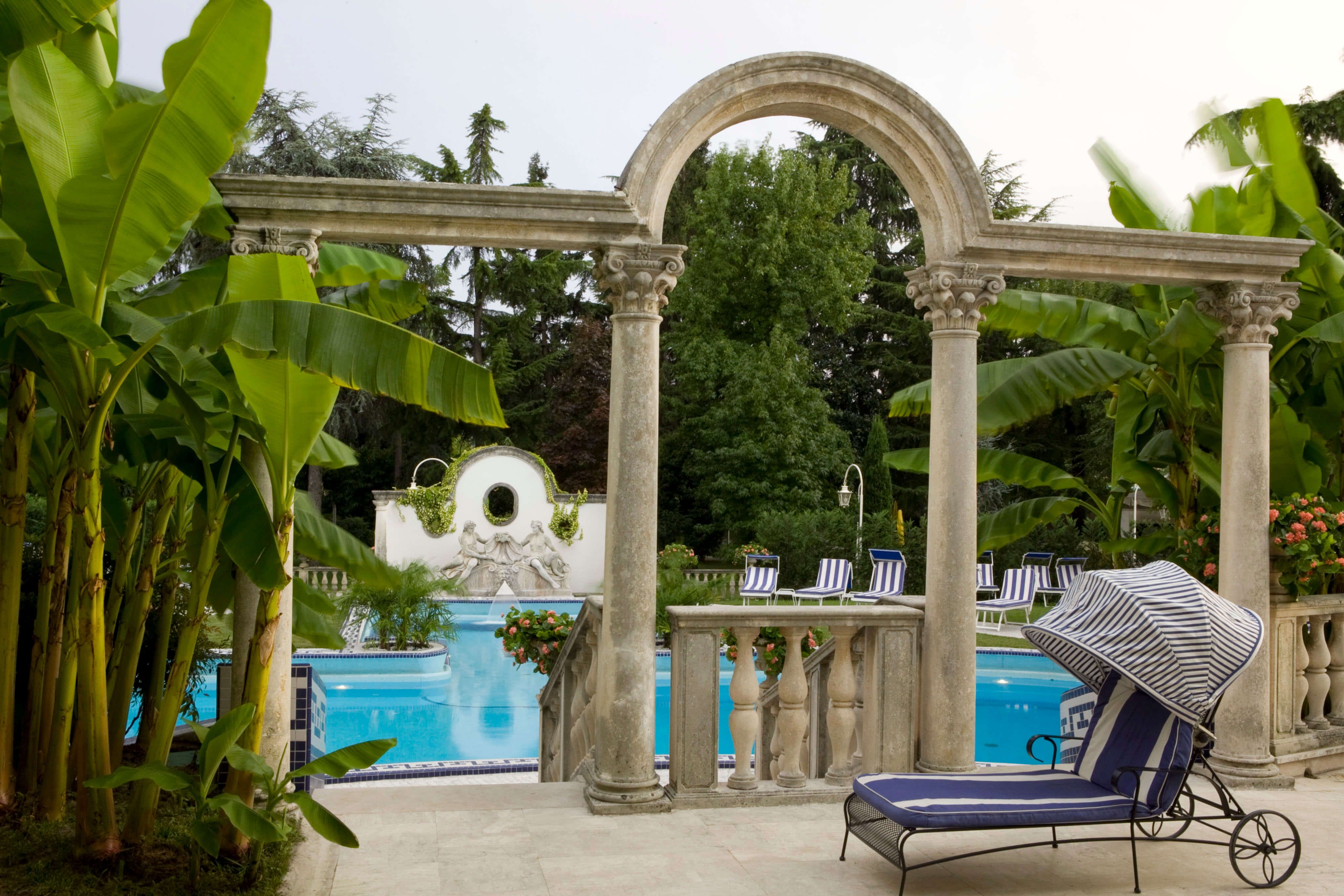 Eine elegante Poollandschaft, umgeben von Palmen und Säulen, mit Liegen zur Entspannung.