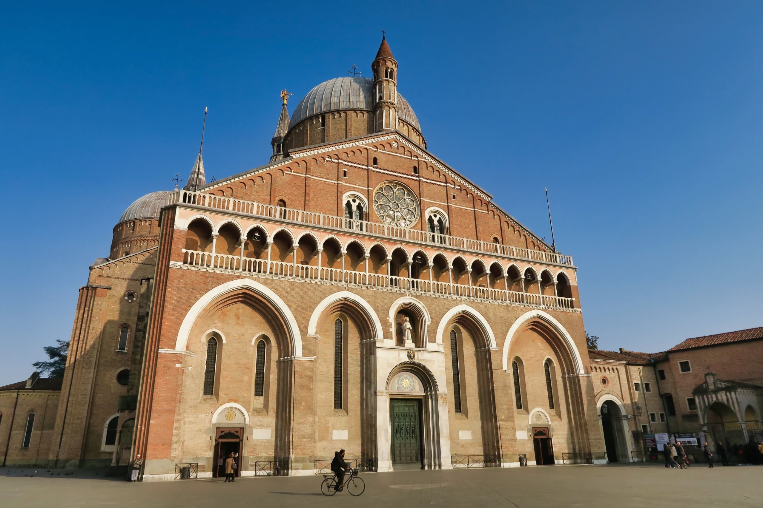 Die Basilika hat eine beeindruckende Fassade mit Rundfenster und Kuppeln, umgeben von blauem Himmel.