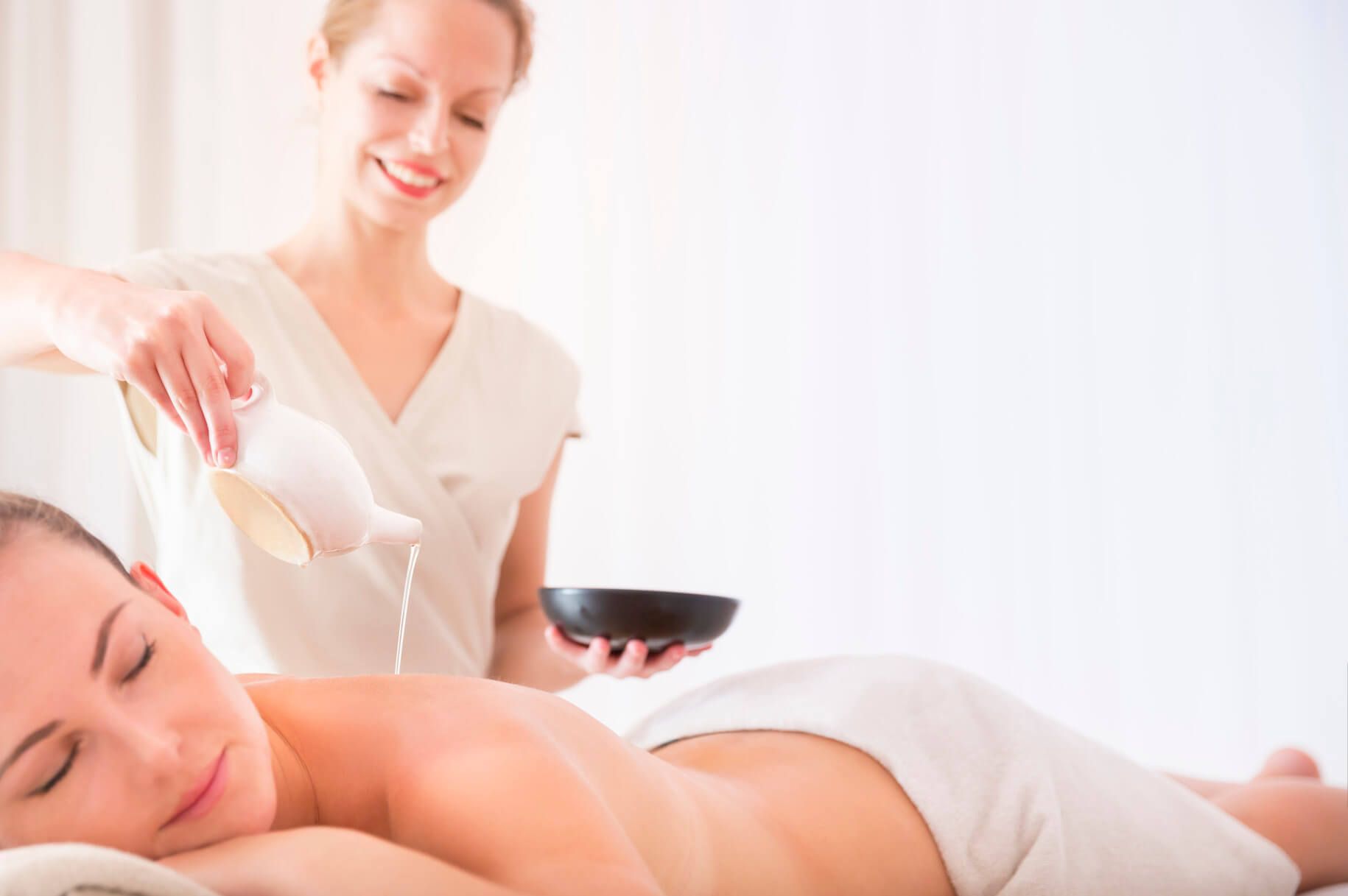 Eine Frau erhält eine Massage, während eine Therapeutin Öl aus einem Krug aufträgt. Entspannung pur!