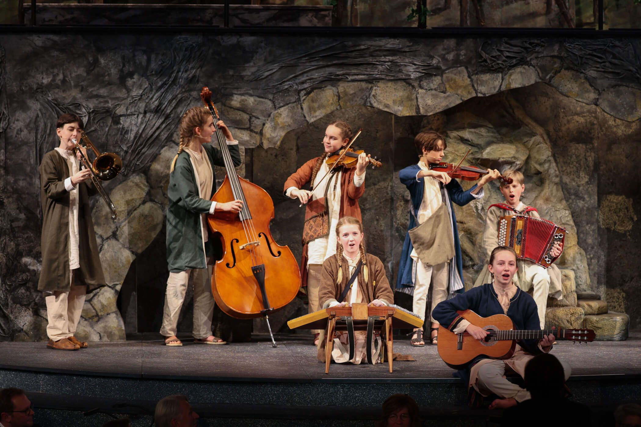 Eine Gruppe junger Musiker spielt auf der Bühne verschiedene Instrumente in einem Theater.