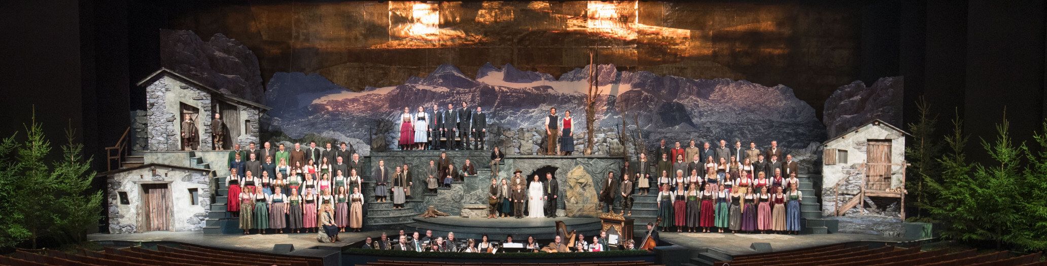 Eine große Bühne mit vielen Darstellern in Trachten und einer beeindruckenden Bergkulisse im Hintergrund.
