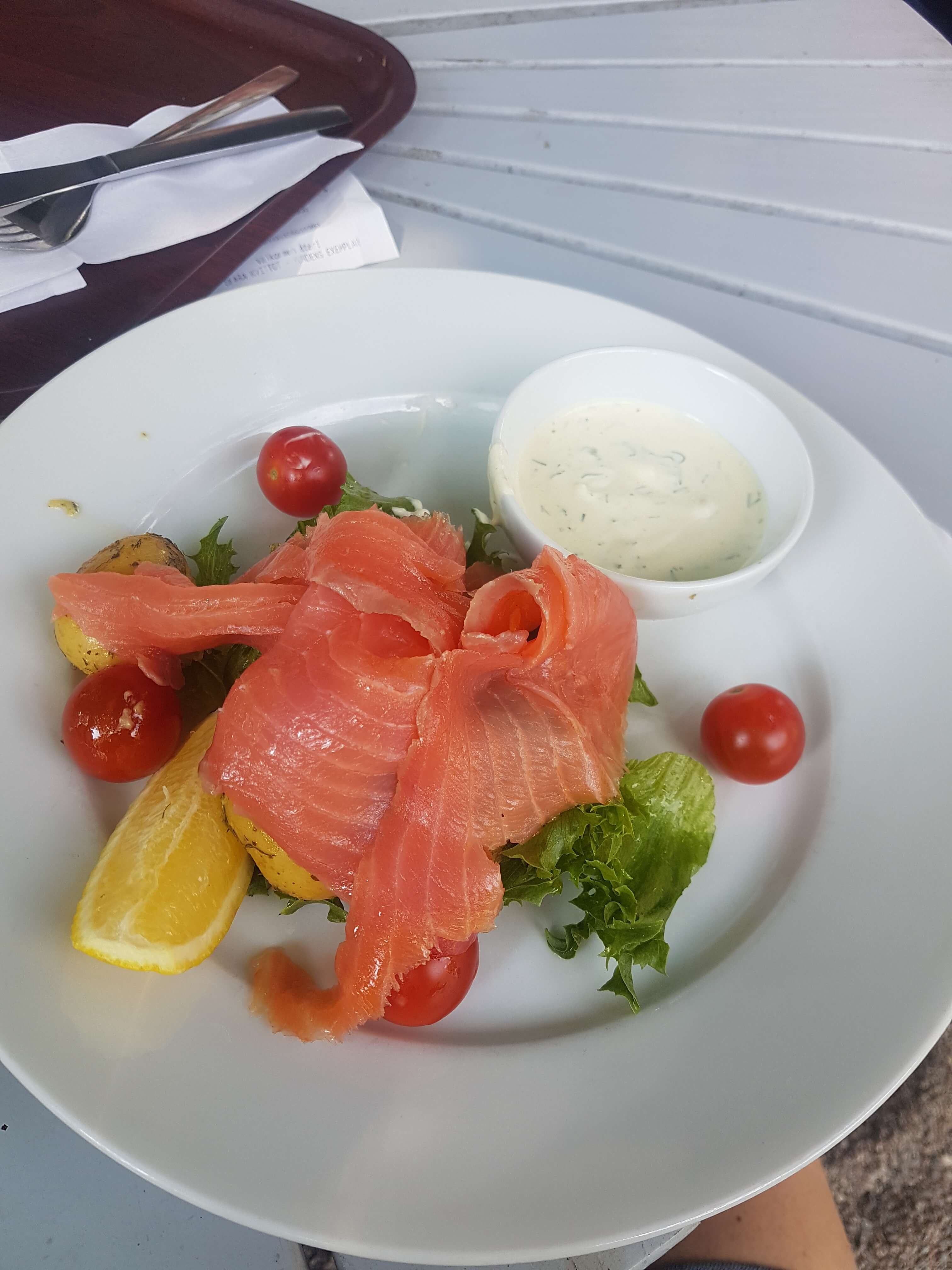Ein Teller mit Räucherlachs, Salat, Kirschtomaten und einer Zitrone, dazu eine Sauce in einer kleinen Schüssel.
