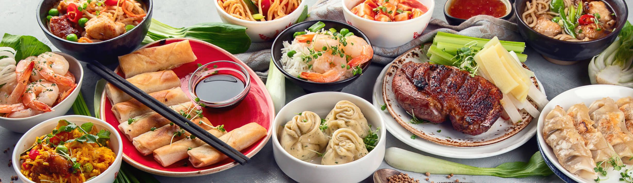 Vielfalt asiatischer Gerichte, darunter Garnelen, Reis, Fleisch und Frühlingsrollen auf einem Tisch angerichtet.