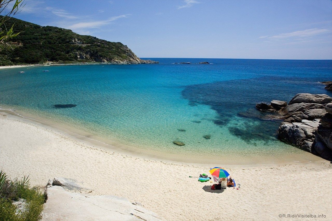 Ein ruhiger Strand auf Elba mit klarem Wasser, sanften Wellen und buntem Sonnenschirm. Ideal für Entspannung und Erholung.