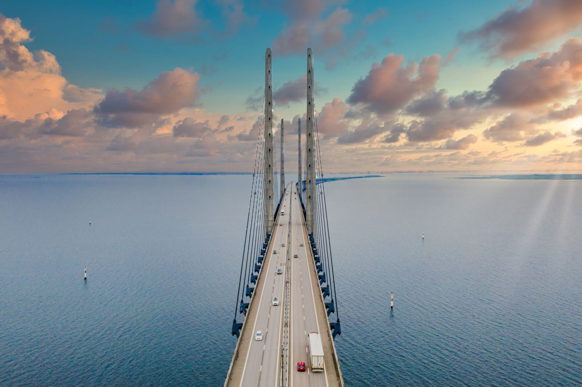 Eine beeindruckende Hängebrücke über ruhigem Wasser, umgeben von Wolken und sanften Farben des Himmels.