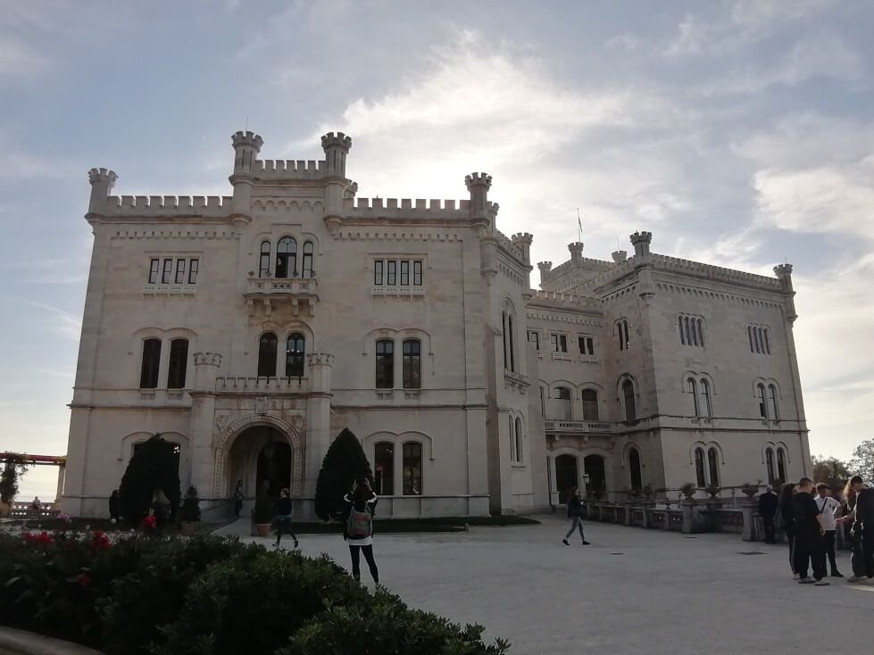 Ein imposantes Schloss mit türmchenartigen Elementen, umgeben von Grün und Besuchern. Traumhafte Architektur.