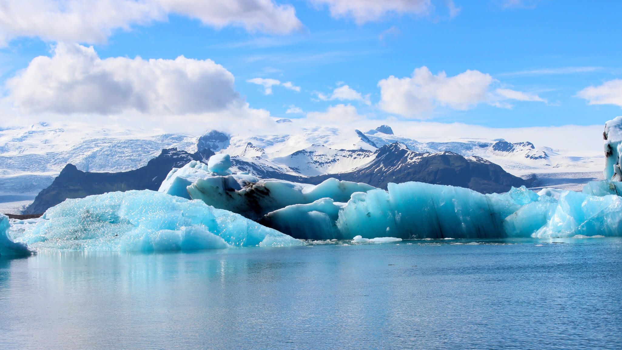 Eine beeindruckende Gletscherlandschaft mit blauen Eisschollen und schneebedeckten Bergen unter einem strahlend blauen Himmel.