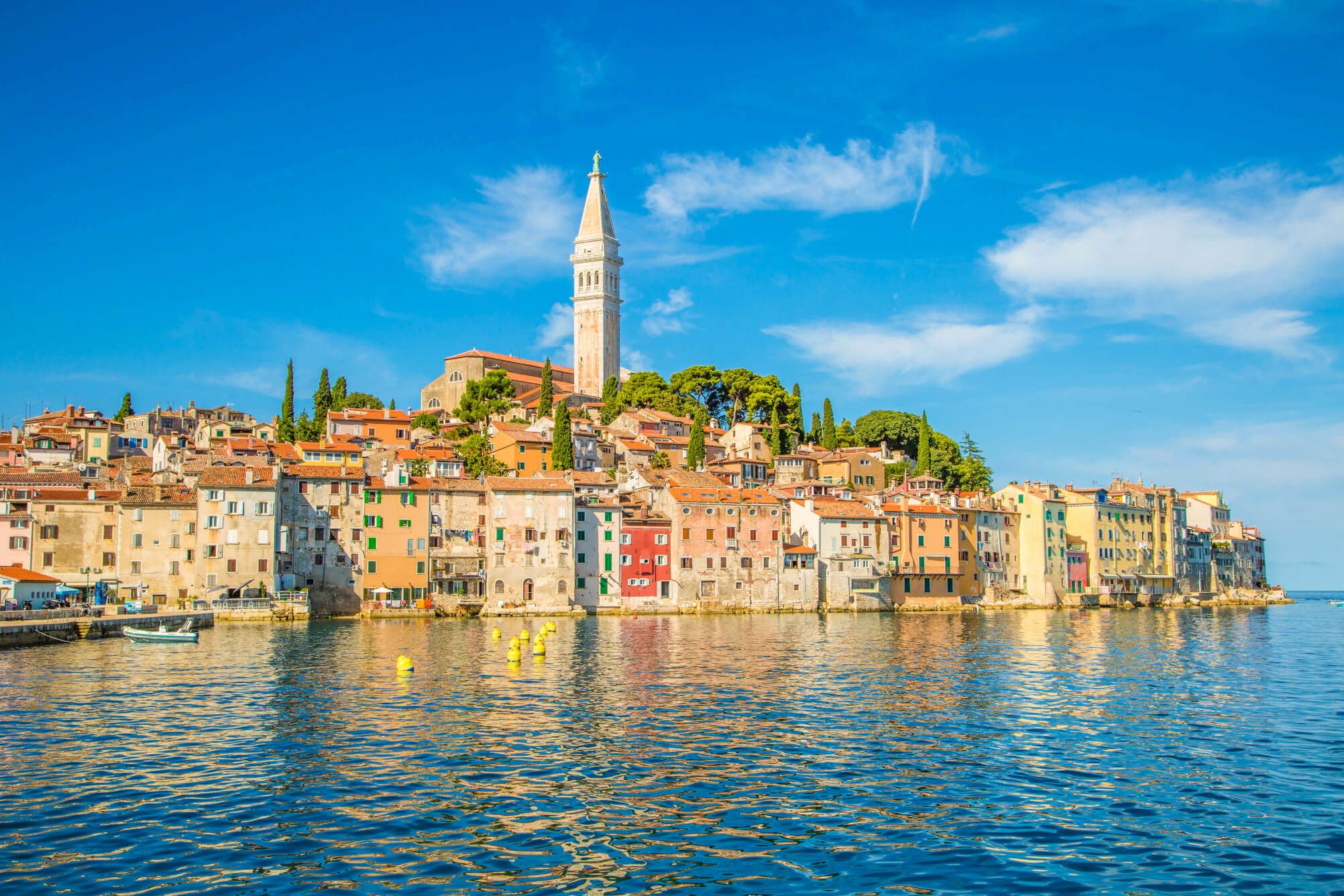 Die malerische Küstenstadt Rovinj mit bunten Häusern und einem Kirchturm unter blauem Himmel.