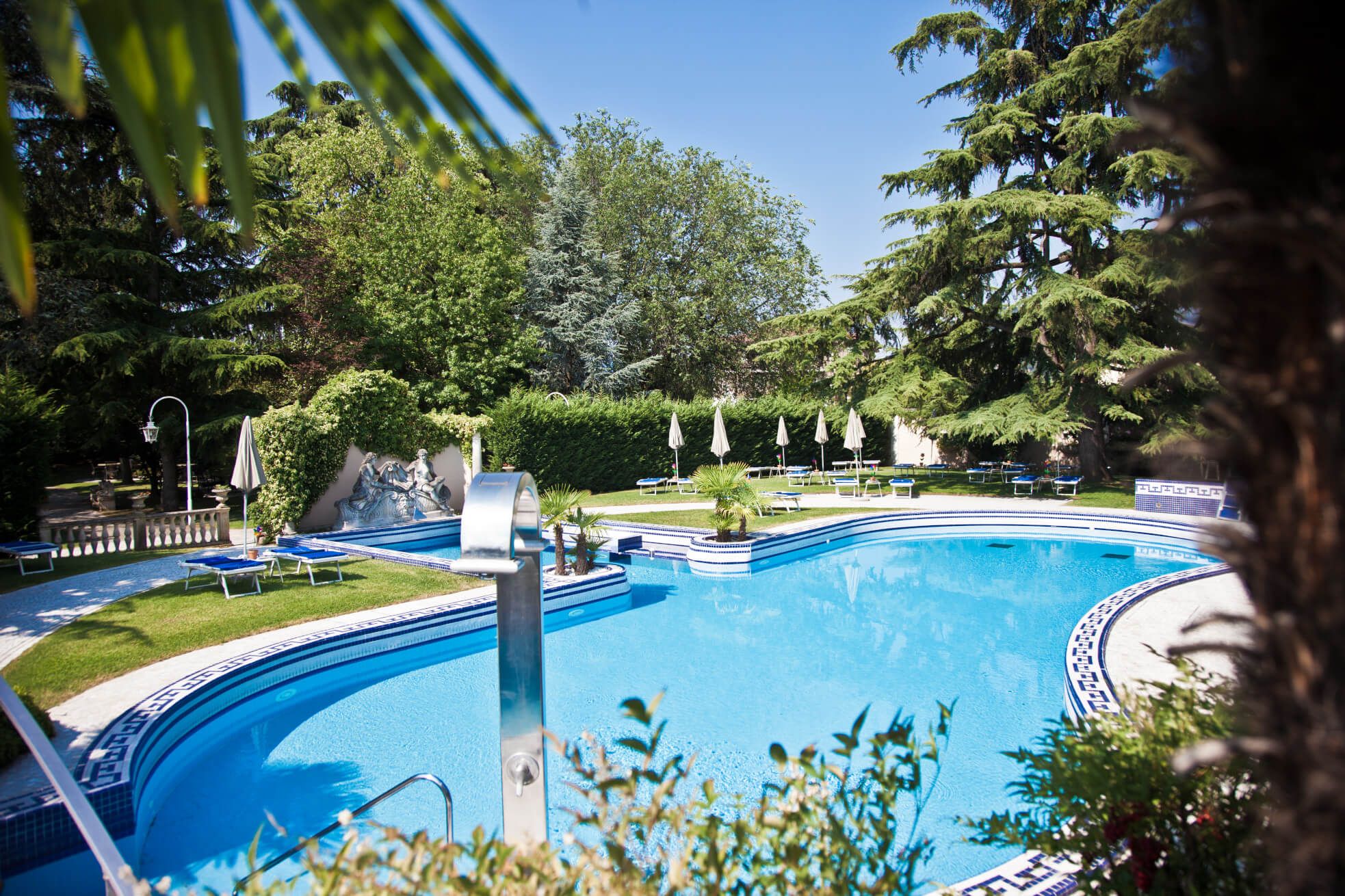 Ein schöner Poolbereich umgeben von Bäumen und Liegen, ideal für Entspannung an einem sonnigen Tag.