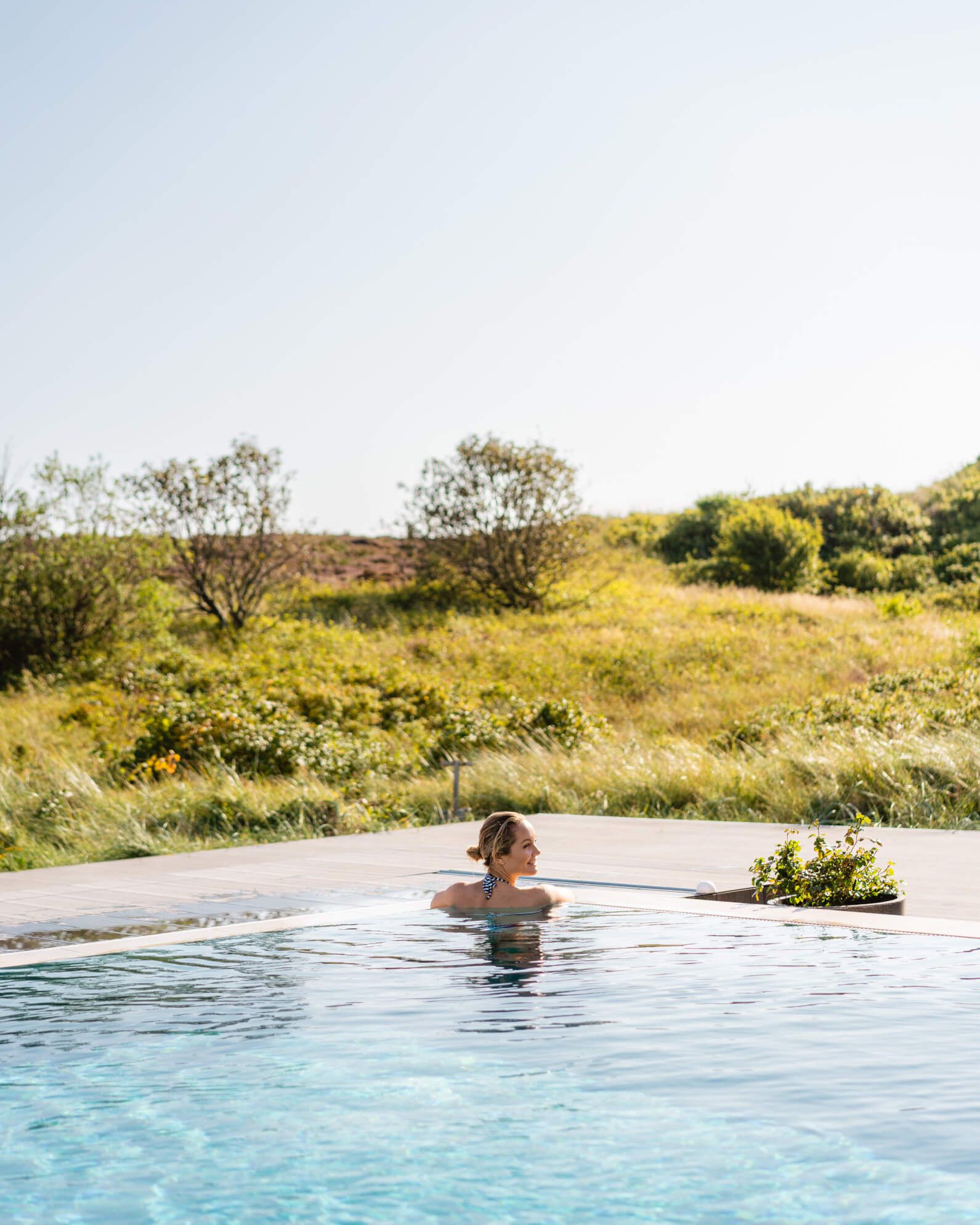 Eine Frau genießt den Nachmittag in einem Pool, umgeben von grünen Wiesen und klarem Himmel.