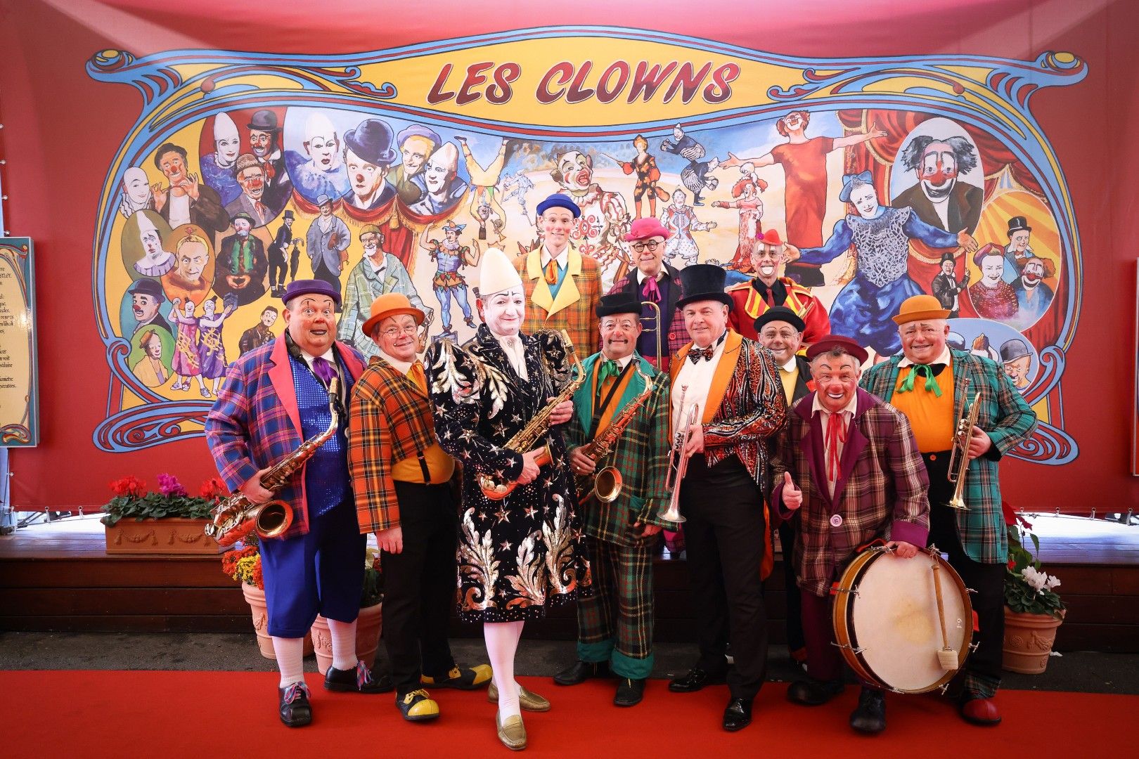 Eine Gruppe von Clowns in bunten Kostümen posiert fröhlich vor einem farbenfrohen Hintergrund.