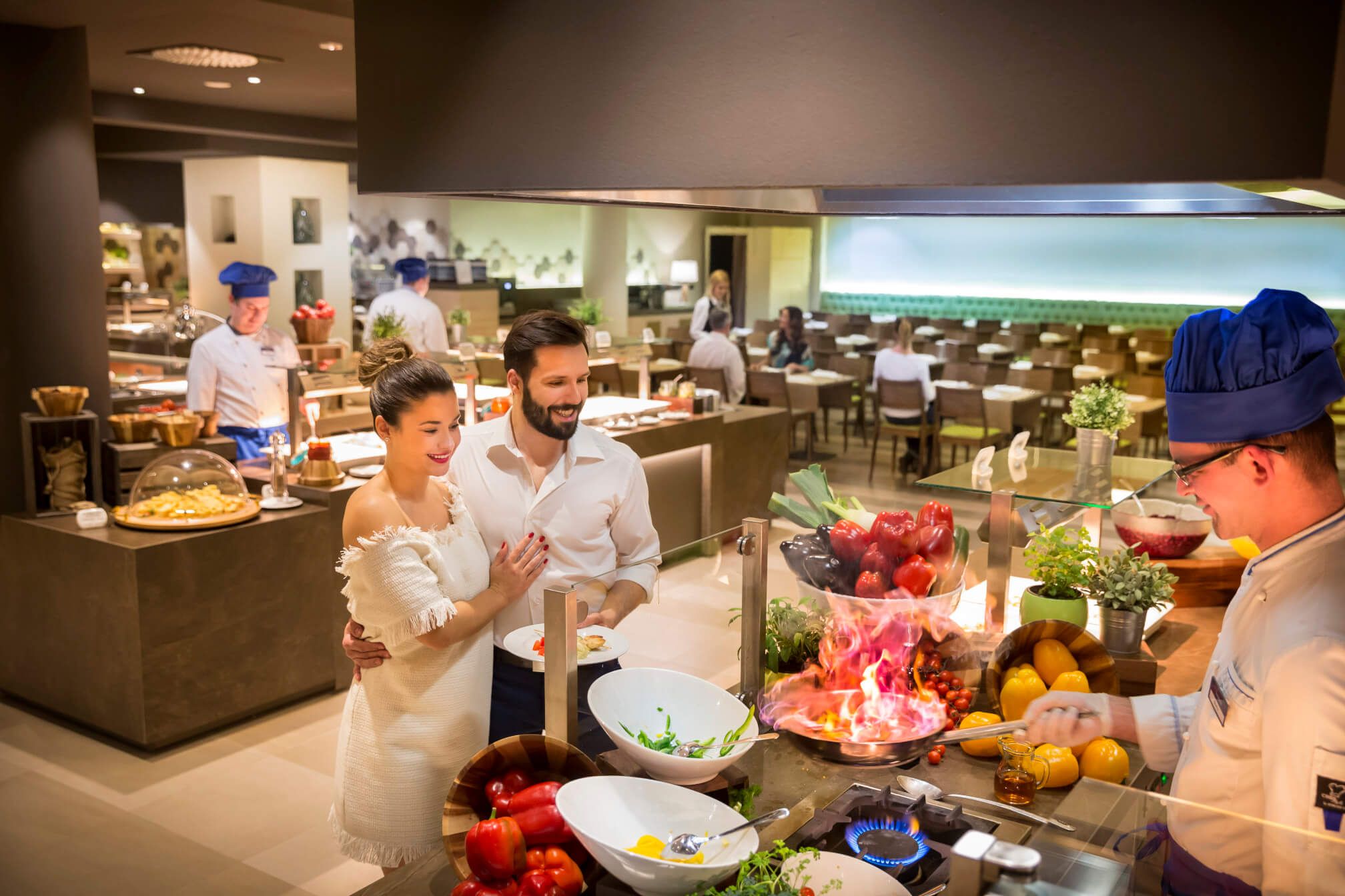 Ein Paar genießt ein Abendessen in einem modernen Restaurant mit offener Küche und Koch, der flambiert.