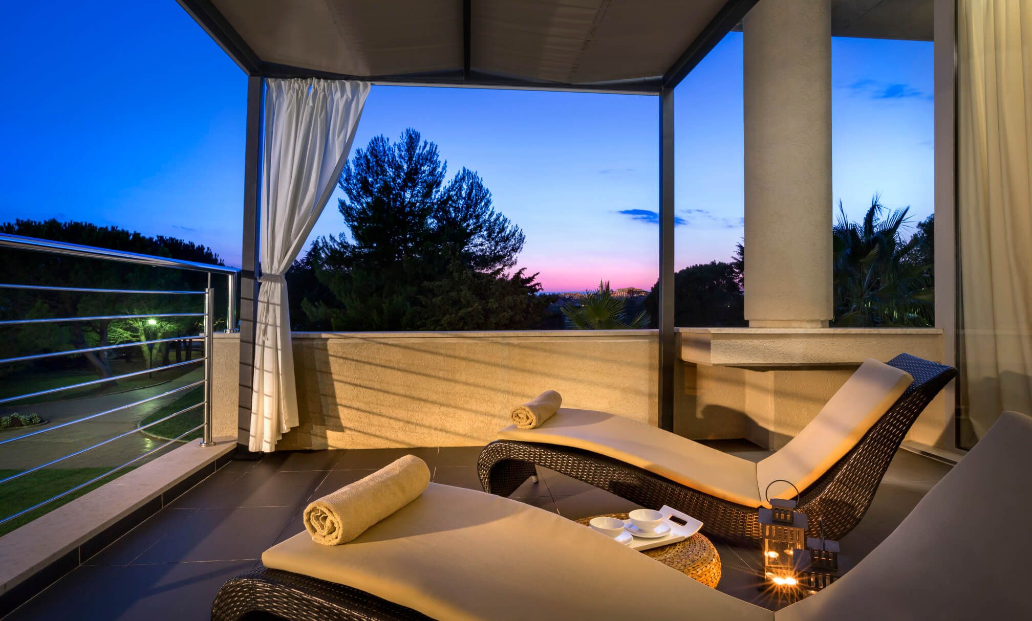 Eine stilvolle Terrasse mit Liegen, Handtüchern und einem zauberhaften Sonnenuntergang im Hintergrund.