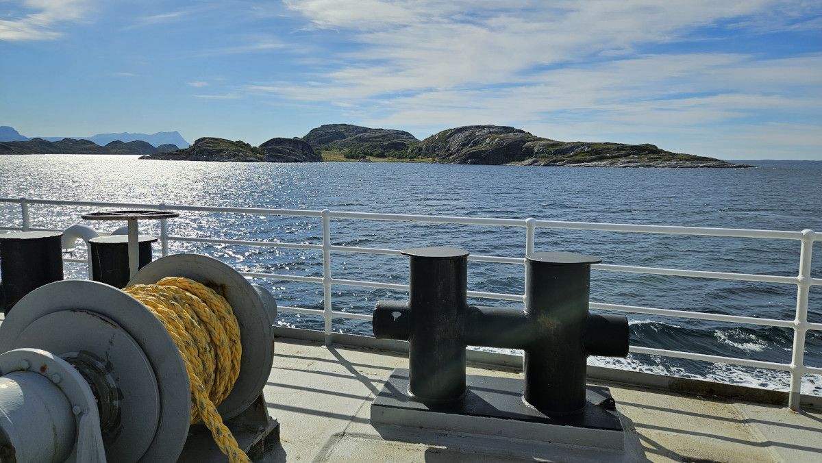 Ein Blick von einem Schiff auf ruhiges Wasser und felsige Inseln unter blauem Himmel.